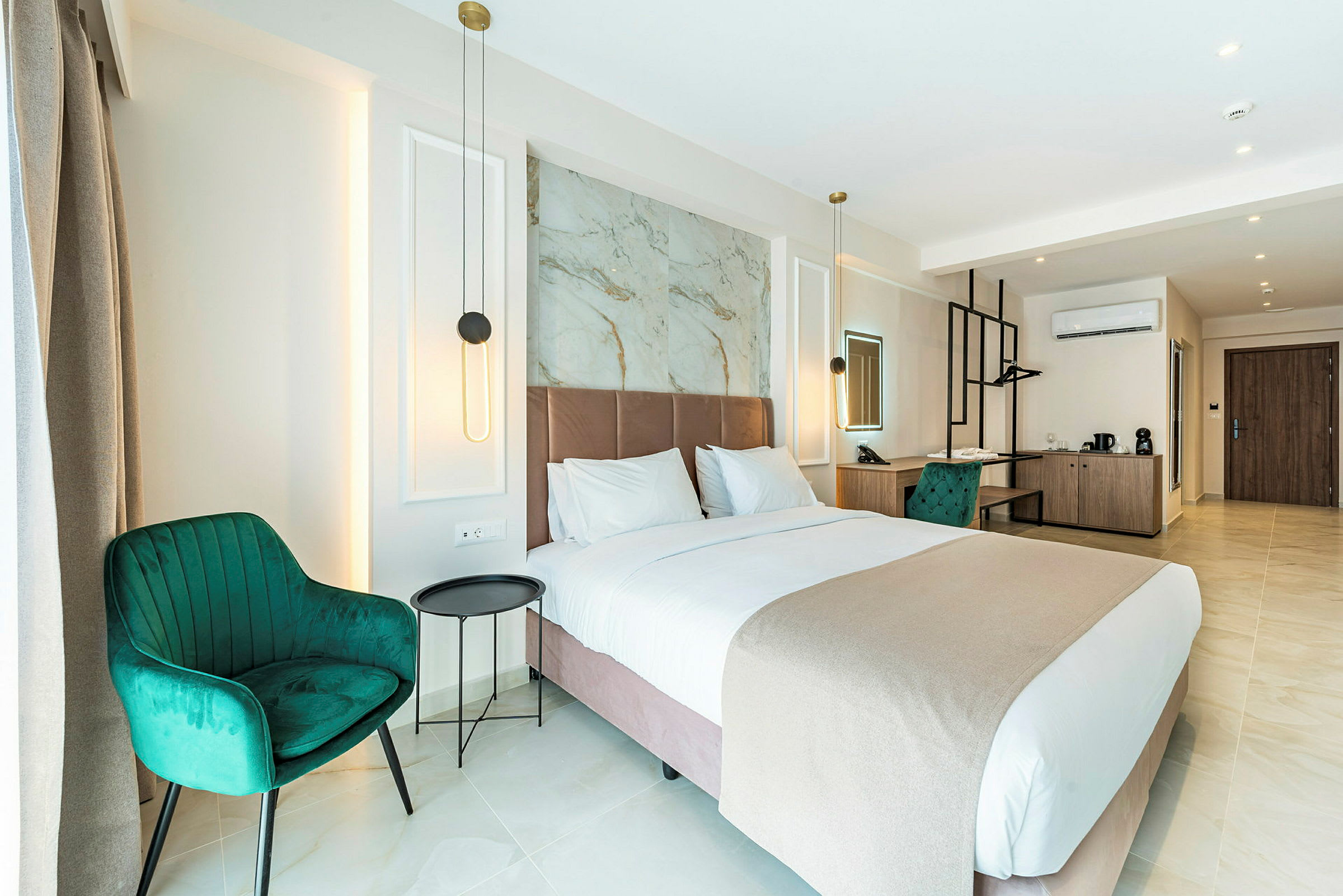 Et moderne hotelværelse med en stor seng, grønne stole og et skrivebord. Værelset er godt oplyst med væglamper og har en stilren indretning. (AI-genereret tekst)