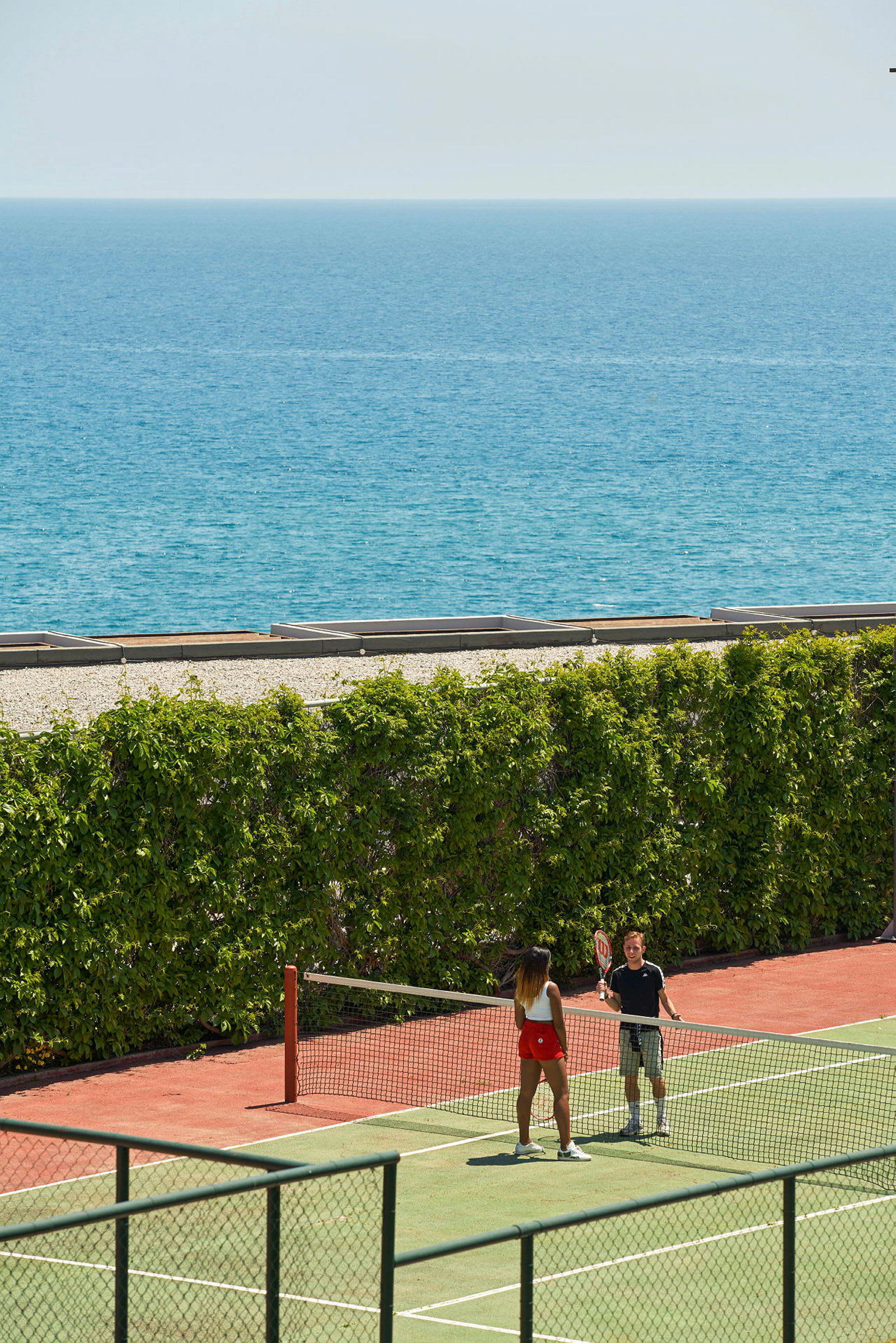 To personer spiller tennis på en tennisbane tæt på havet. (AI-genereret tekst)