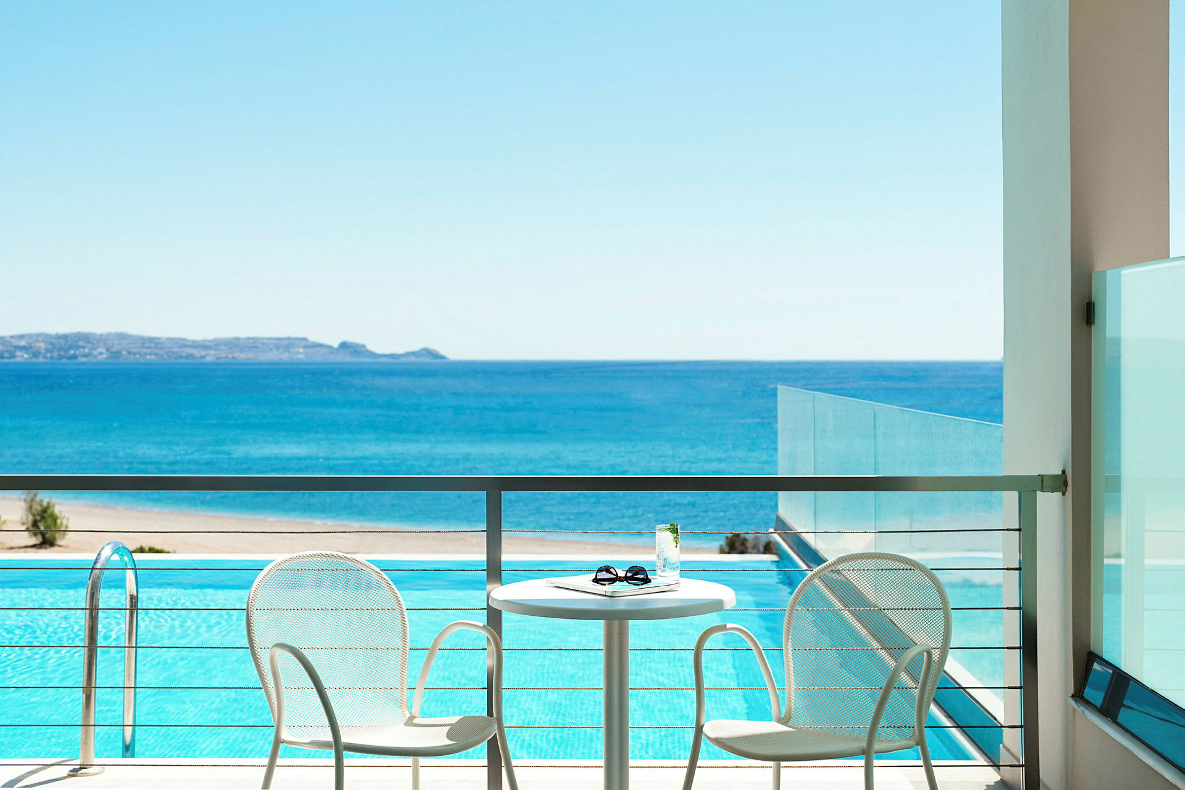 Terrasse med to stole og et bord med udsigt over havet og en pool. (AI-genereret tekst)