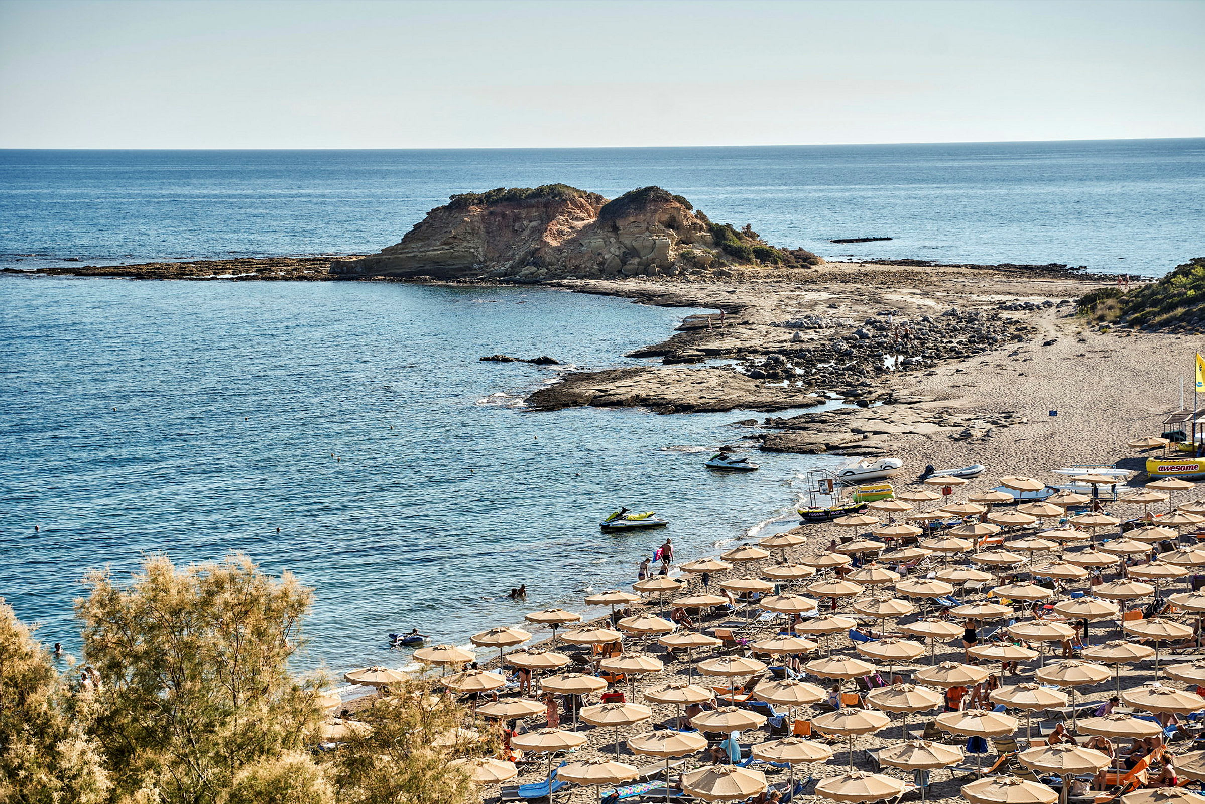 Liggestole og parasoller på en strand ved kysten med klipper og hav. (AI-genereret tekst)