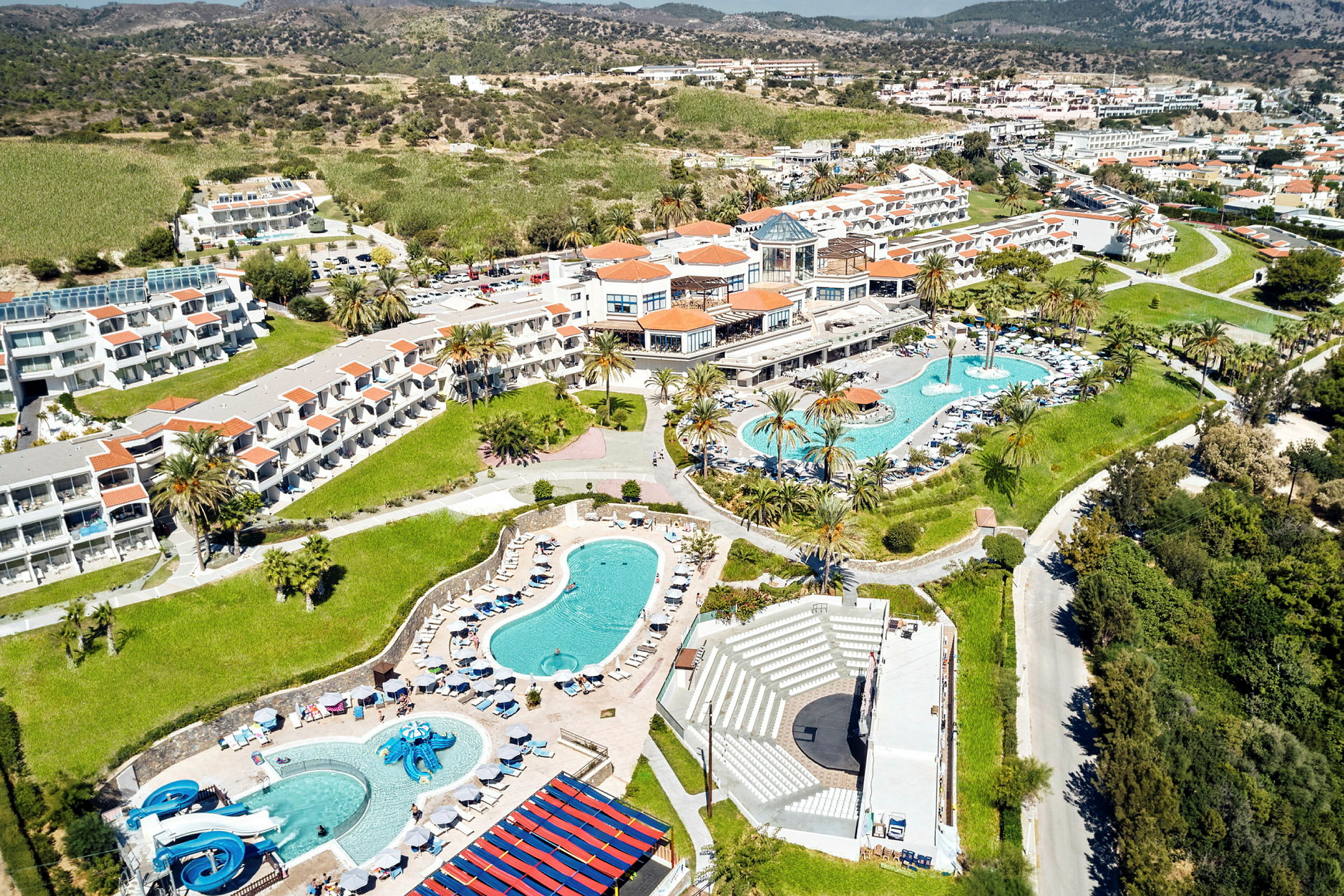 Luftfoto af en resort med pools, bygninger og grønne områder. (AI-genereret tekst)