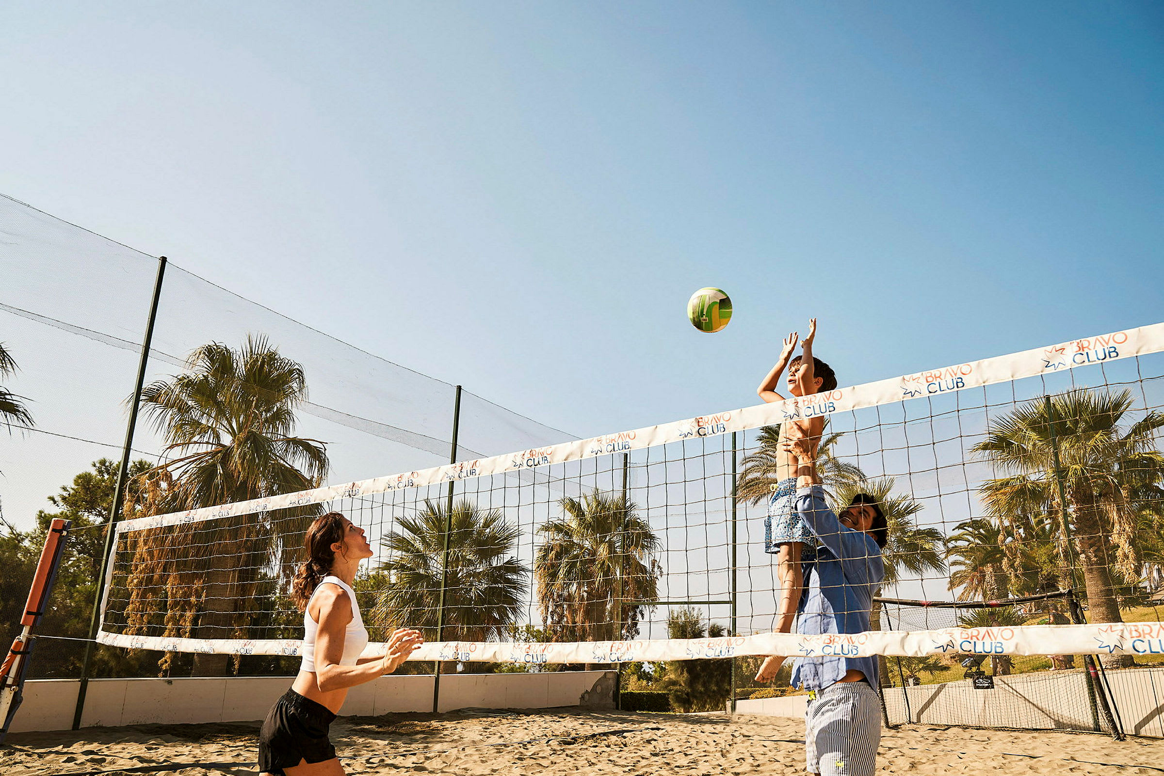 Personer spiller volleyball på en sandbane med palmer i baggrunden. (AI-genereret tekst)