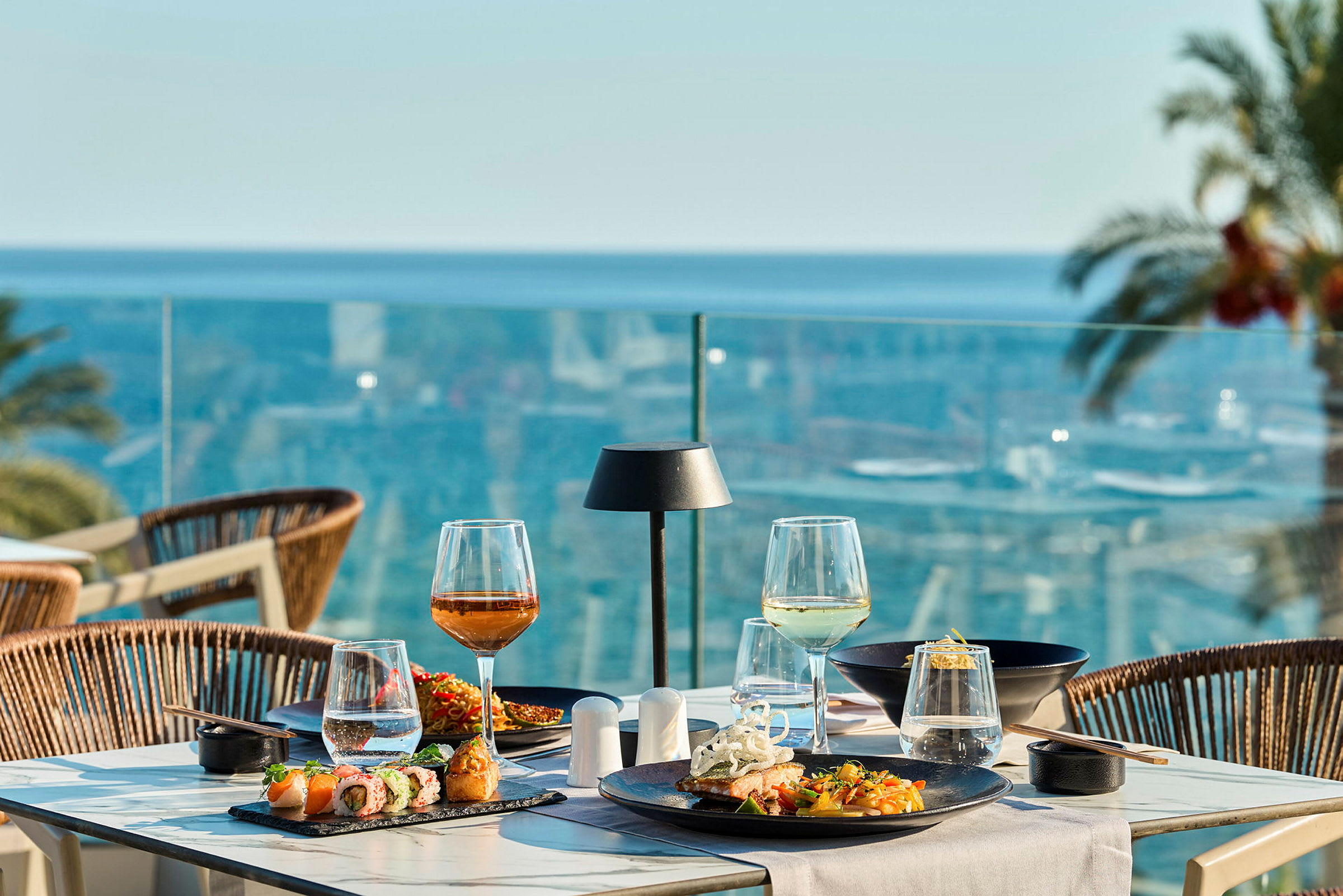 Et dækket bord med mad og drikke på en terrasse med udsigt over havet. (AI-genereret tekst)