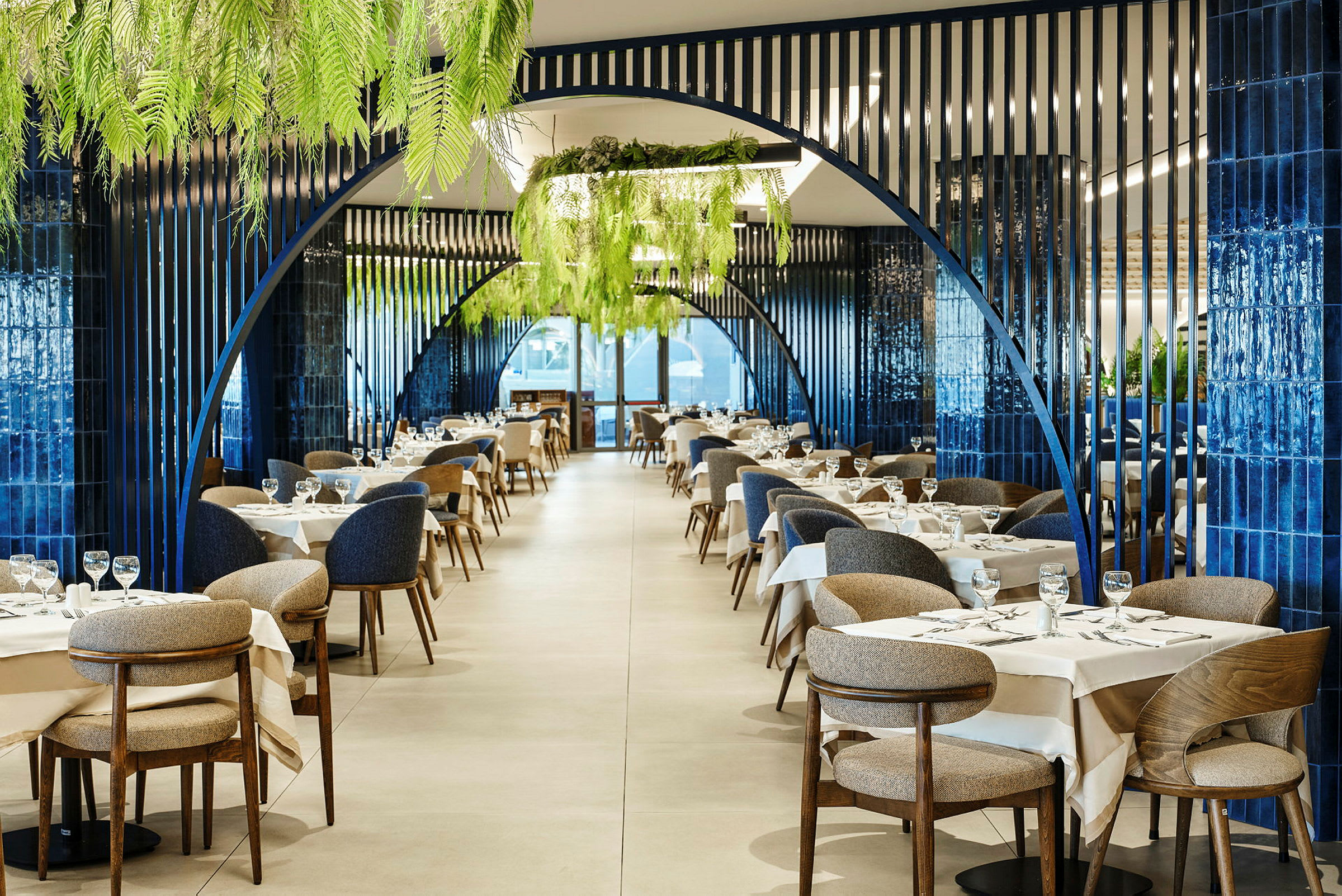 En elegant indrettet restaurant med blå buestrukturer, hvide duge og grønne planter i loftet. (AI-genereret tekst)