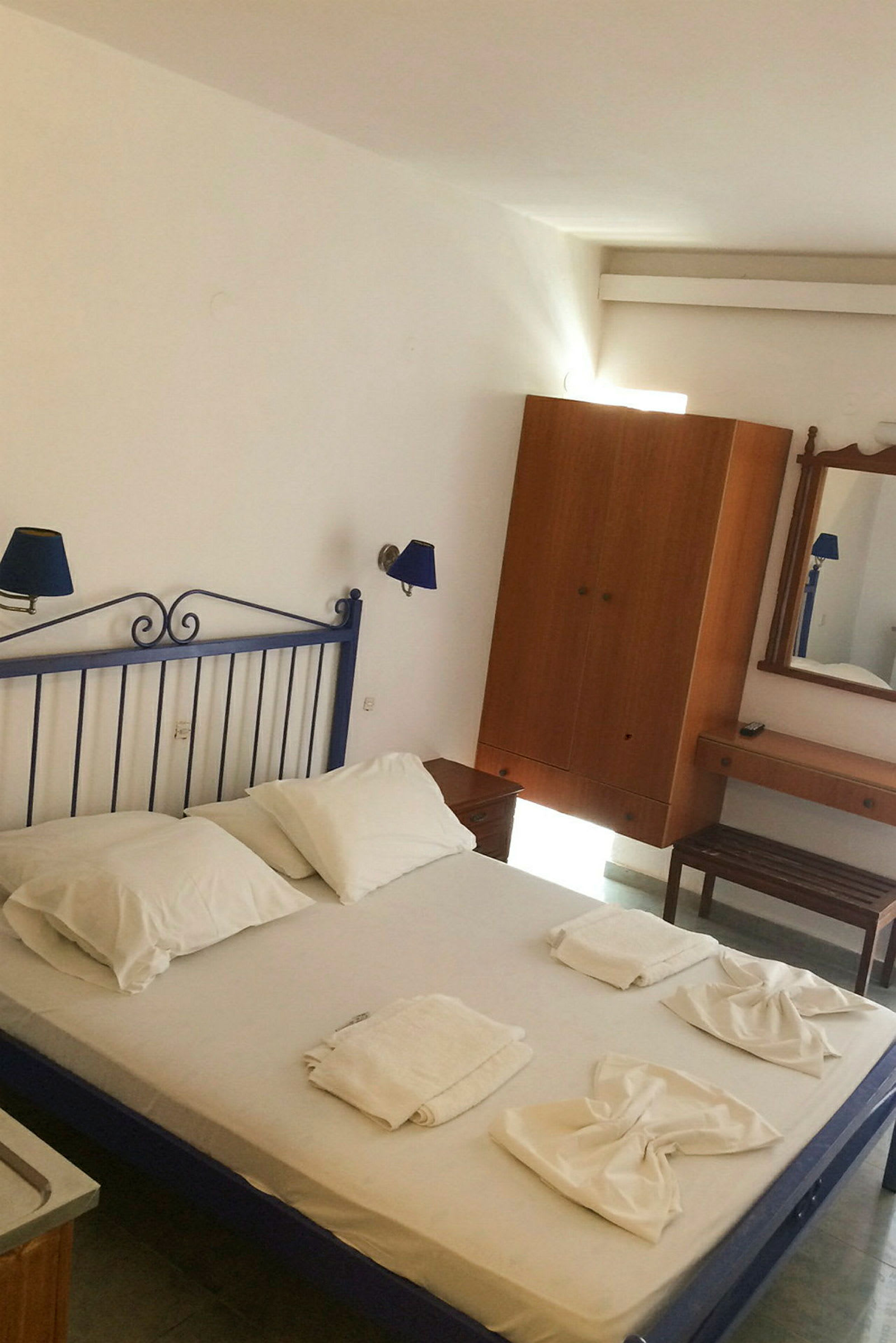Et hotelværelse med en seng med hvidt sengetøj, håndklæder arrangeret på sengen og møbler, herunder garderobe og spejl. (AI-genereret tekst)