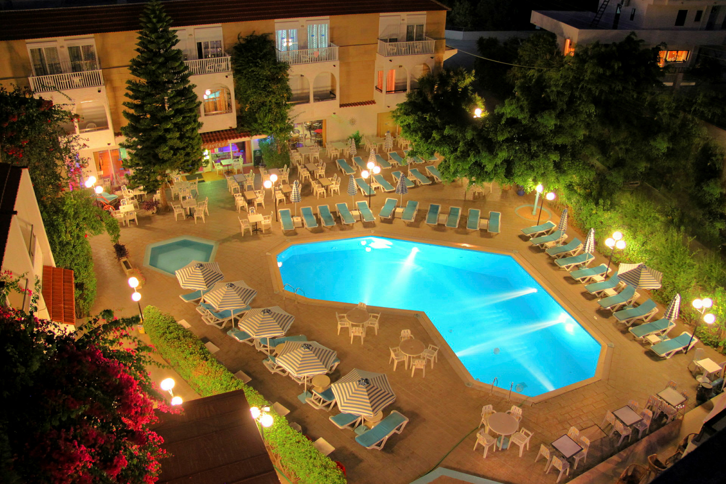 Billede af en hotelpool med liggestole og parasoller omkring, aftenbelysning skaber en varm atmosfære. (AI-genereret tekst)