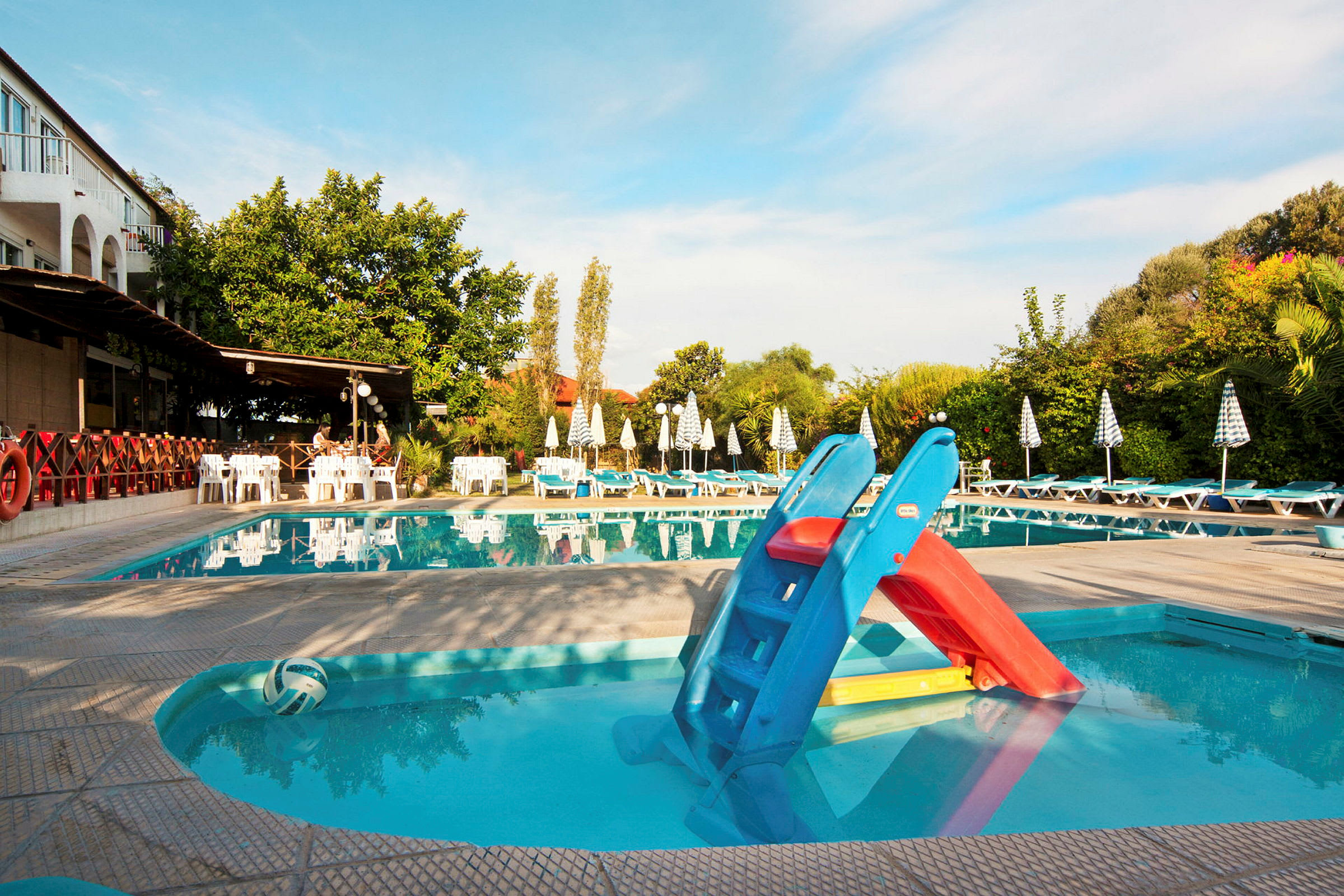 Billede af en swimmingpool med liggestole og parasoller omkring. En lille vandrutsjebane er placeret ved poolkanten. (AI-genereret tekst)