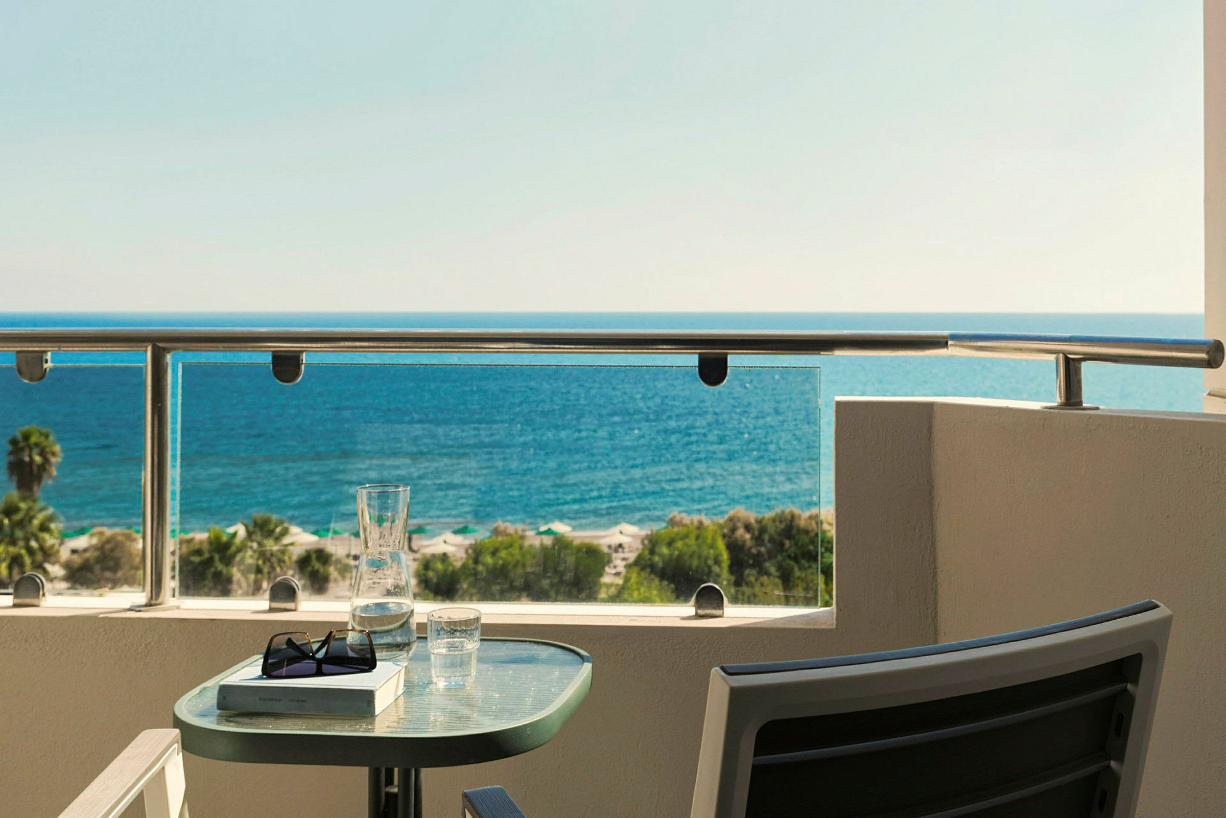 Udsigt over havet fra en balkon med et bord med glas og bog placeret på. (AI-genereret tekst)