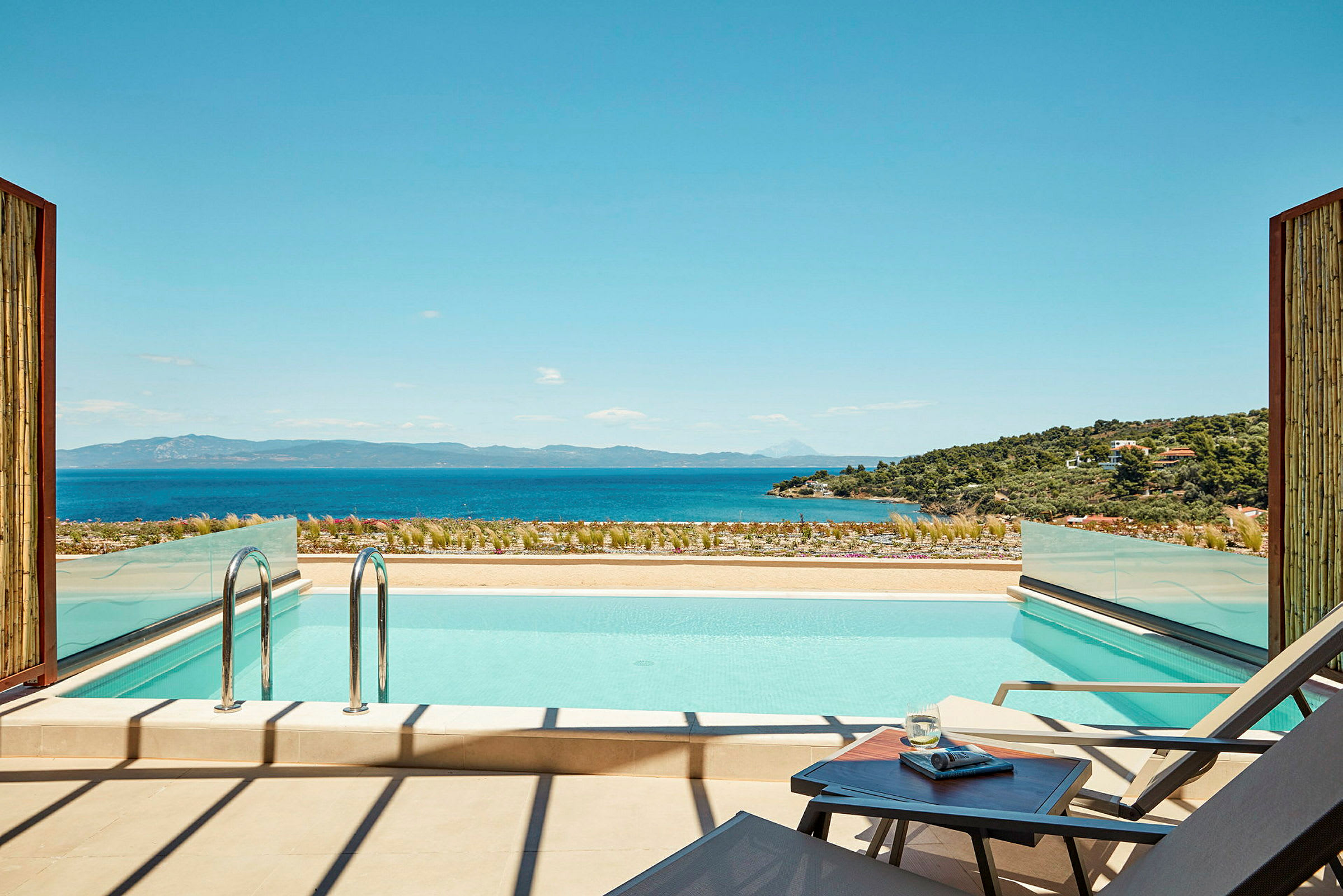 En moderne udendørs swimmingpool med udsigt over havet og et frodigt landskab. (AI-genereret tekst)
