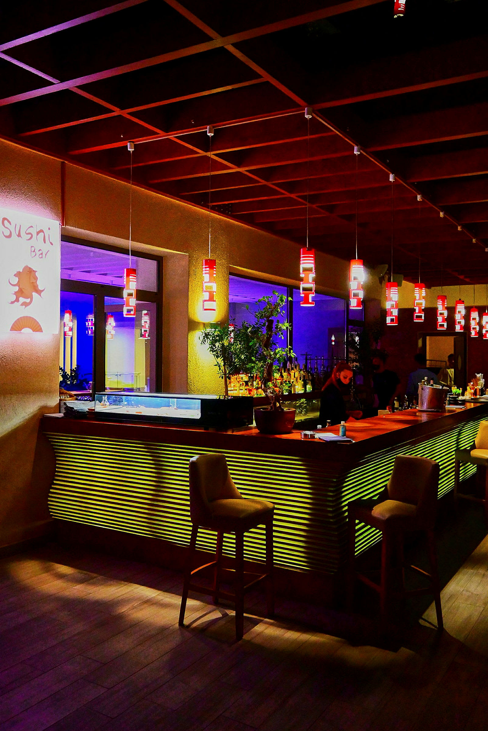 En moderne sushi-bar med hyggelig belysning og stole omkring bardisken. (AI-genereret tekst)
