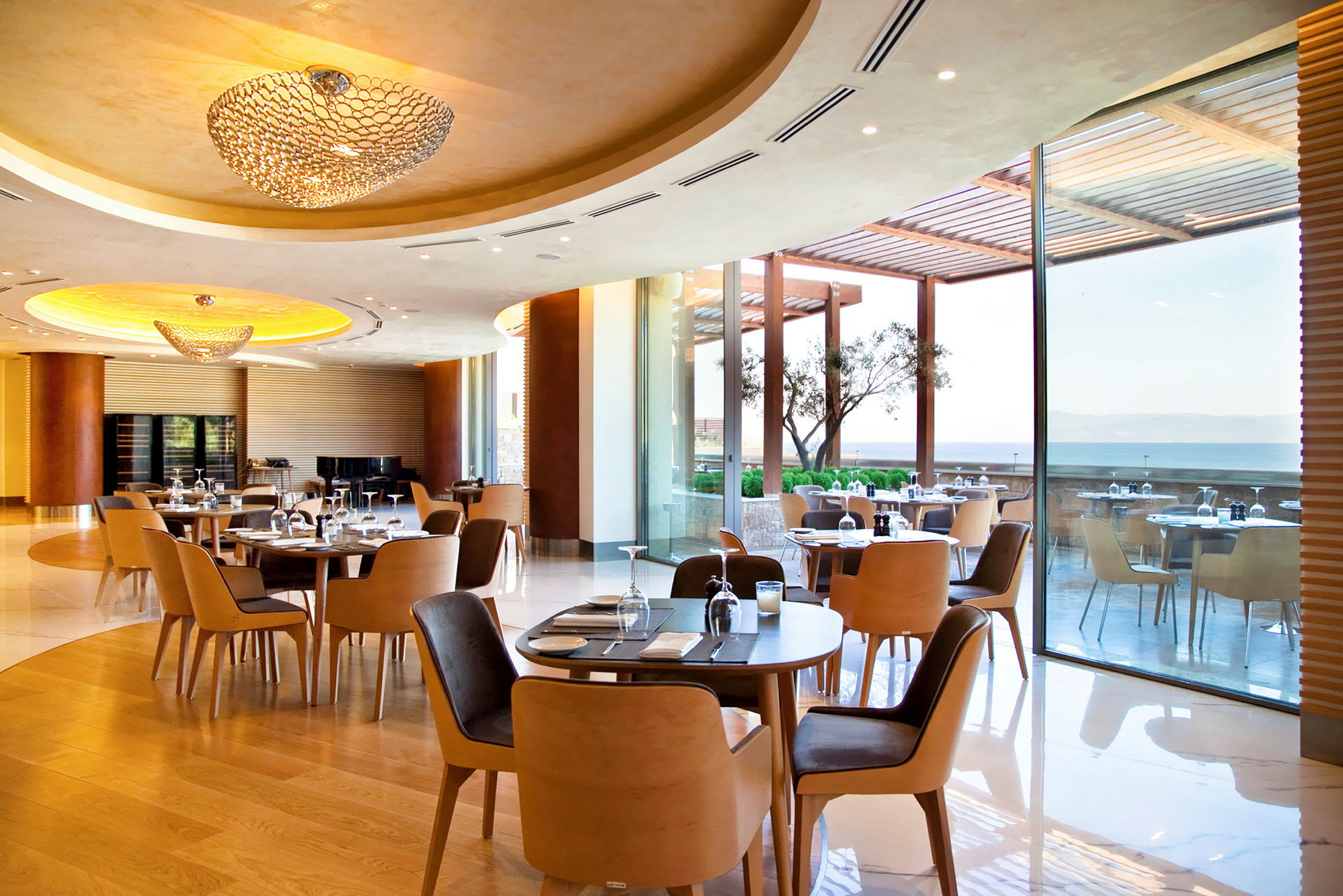 En rummelig restaurant med moderne møbler og store vinduer, der vender ud mod en terrasse med havudsigt. (AI-genereret tekst)