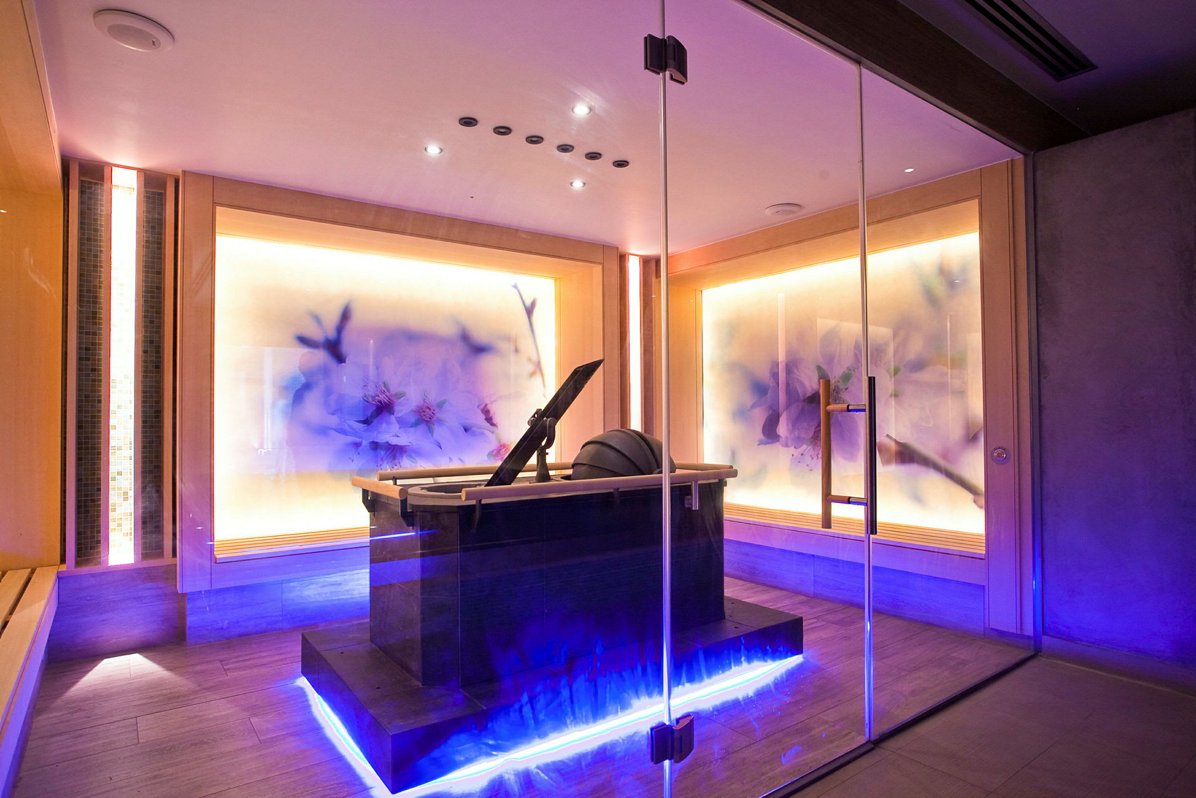 Et moderne spa-rum med glasvægge, blomstrende lyspaneler og en central vandinstallation (AI-genereret tekst)