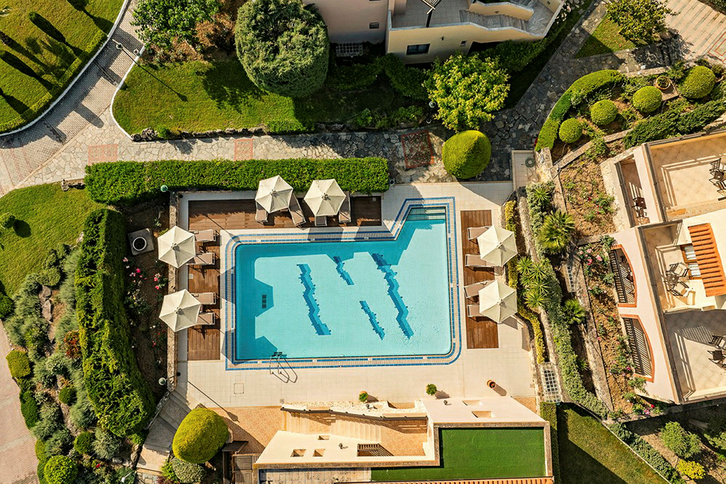 Luftfoto af en bygning med swimmingpool og omkringliggende grønne områder. (AI-genereret tekst)