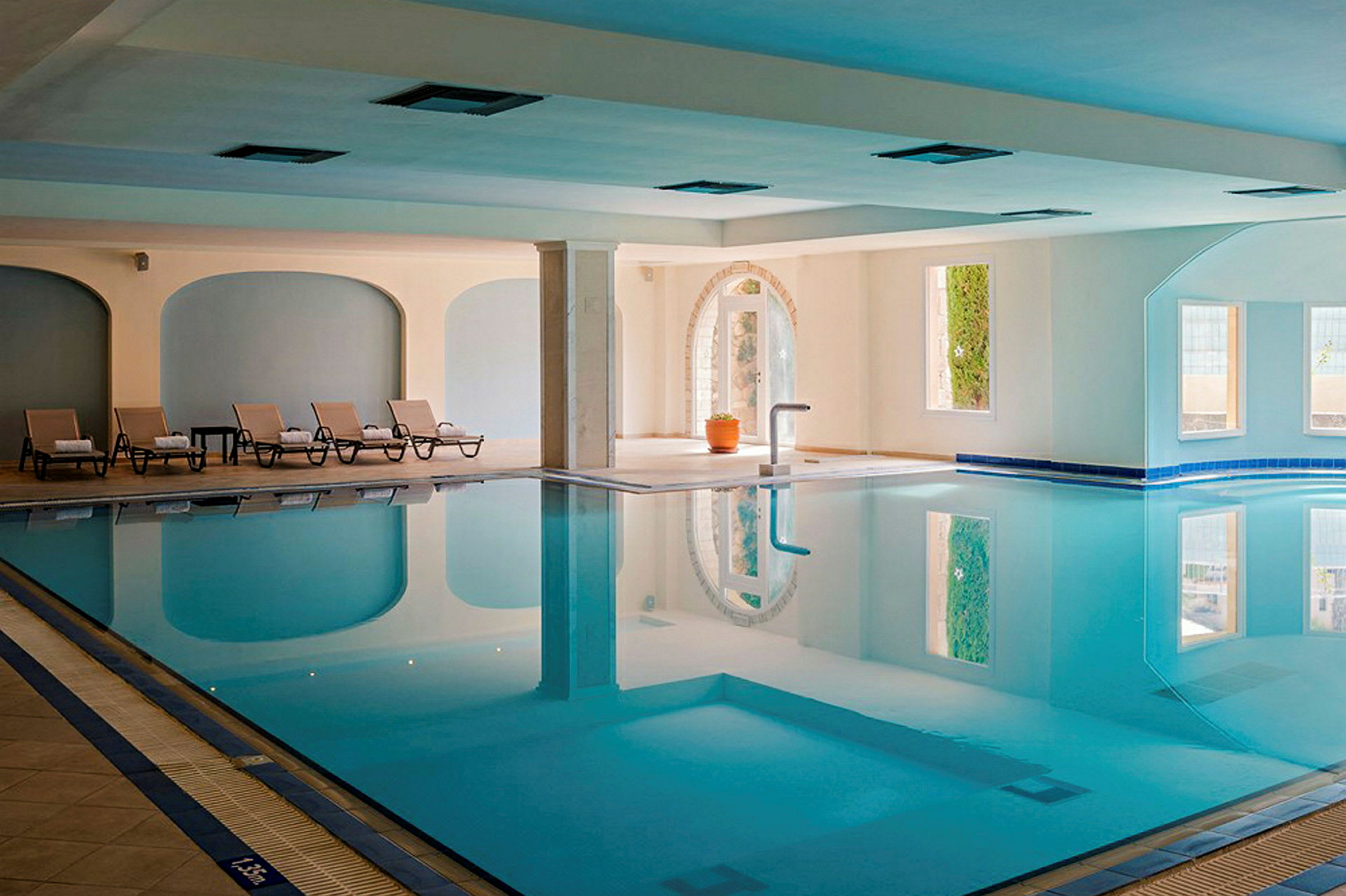 En indendørs pool med liggestole placeret langs den ene side. (AI-genereret tekst)