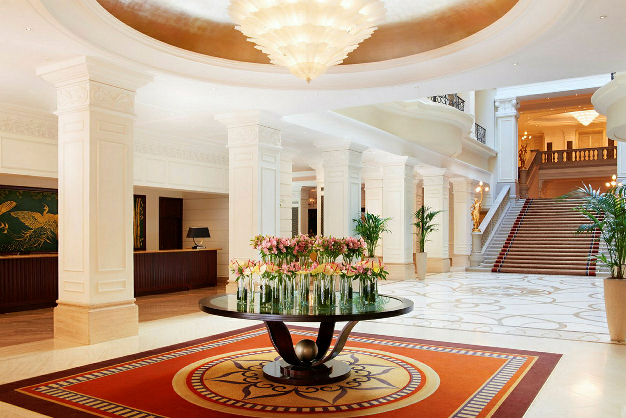 En elegant hotellobby med marmorgulv, et centerbord dekoreret med blomster og en trappe i baggrunden. (AI-genereret tekst)