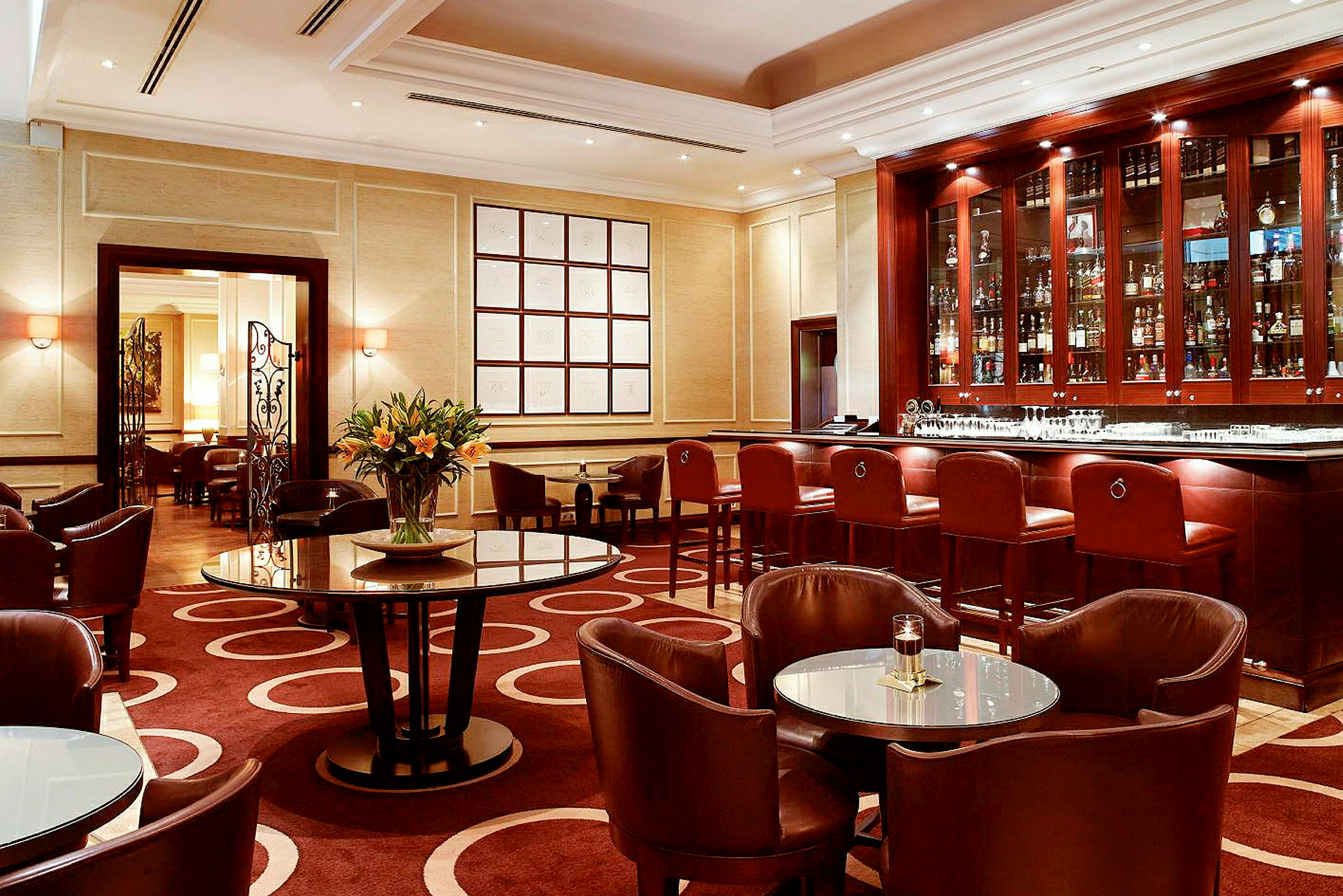 En elegant hotellbar med mørke trædetaljer, flere borde og stole samt en blomst i midten. (AI-genereret tekst)