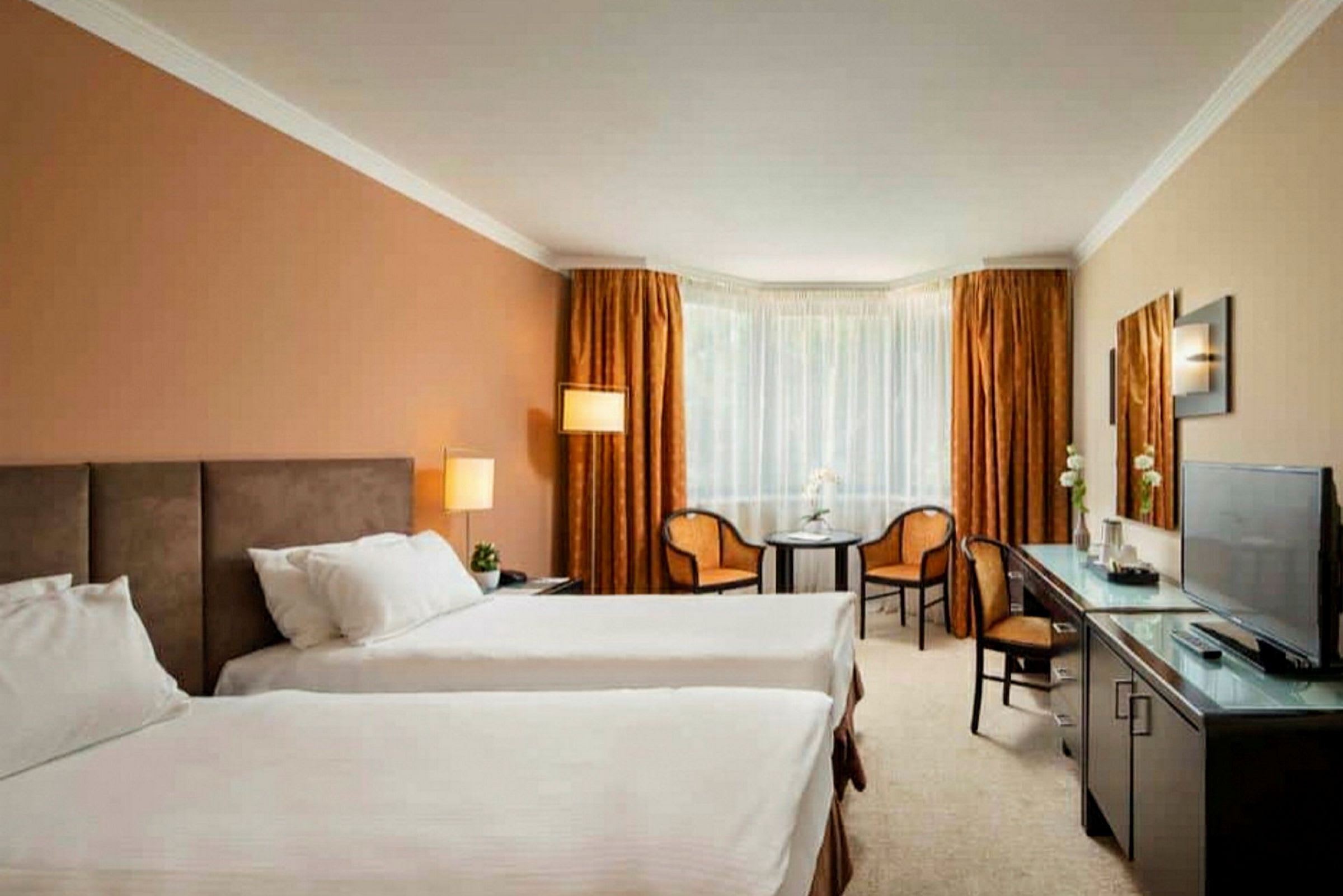 Hotelværelse med to enkeltsenge, et bord, to stole og et fjernsyn. (AI-genereret tekst)