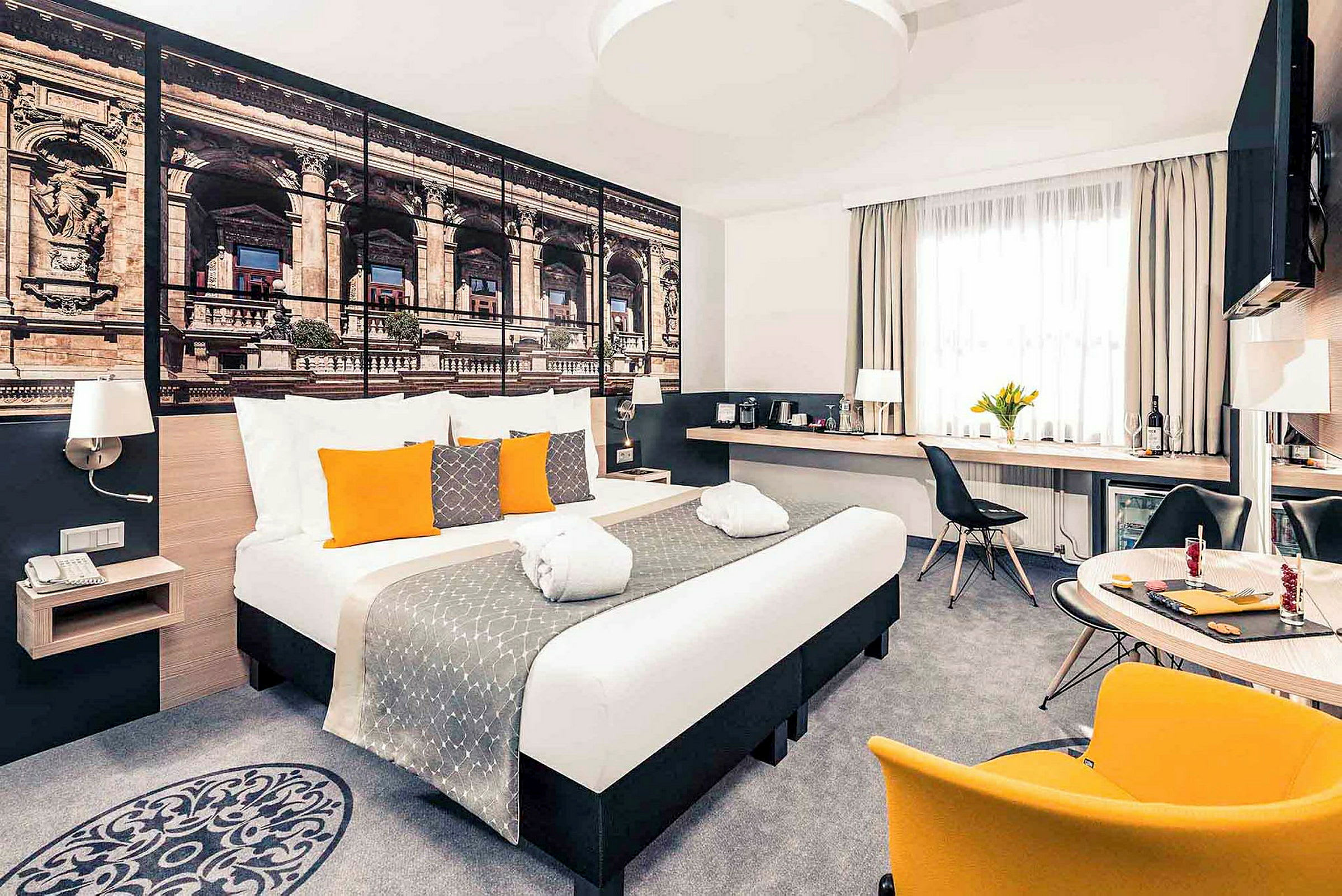 Moderne hotelværelse med dobbeltseng, dekorative puder og et stort vægbillede af arkitektur. (AI-genereret tekst)