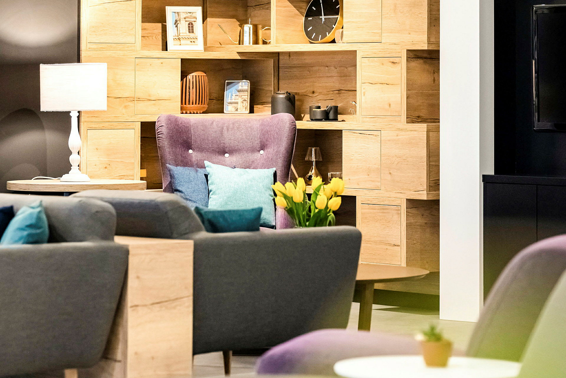 En stue med en bogreol, lænestol, sofaer og dekorative genstande, herunder en vase med gule tulipaner. (AI-genereret tekst)