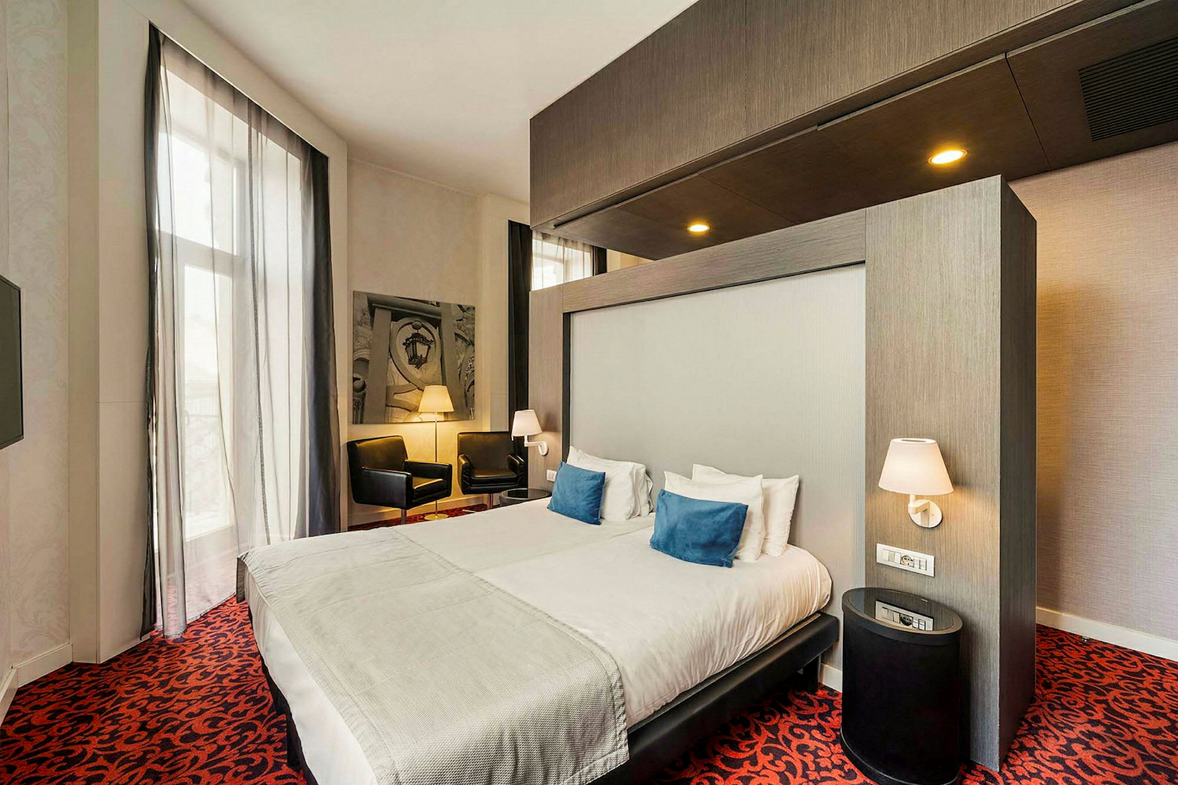 Et moderne hotelværelse med dobbeltseng, natbord og siddeområde med stole. (AI-genereret tekst)