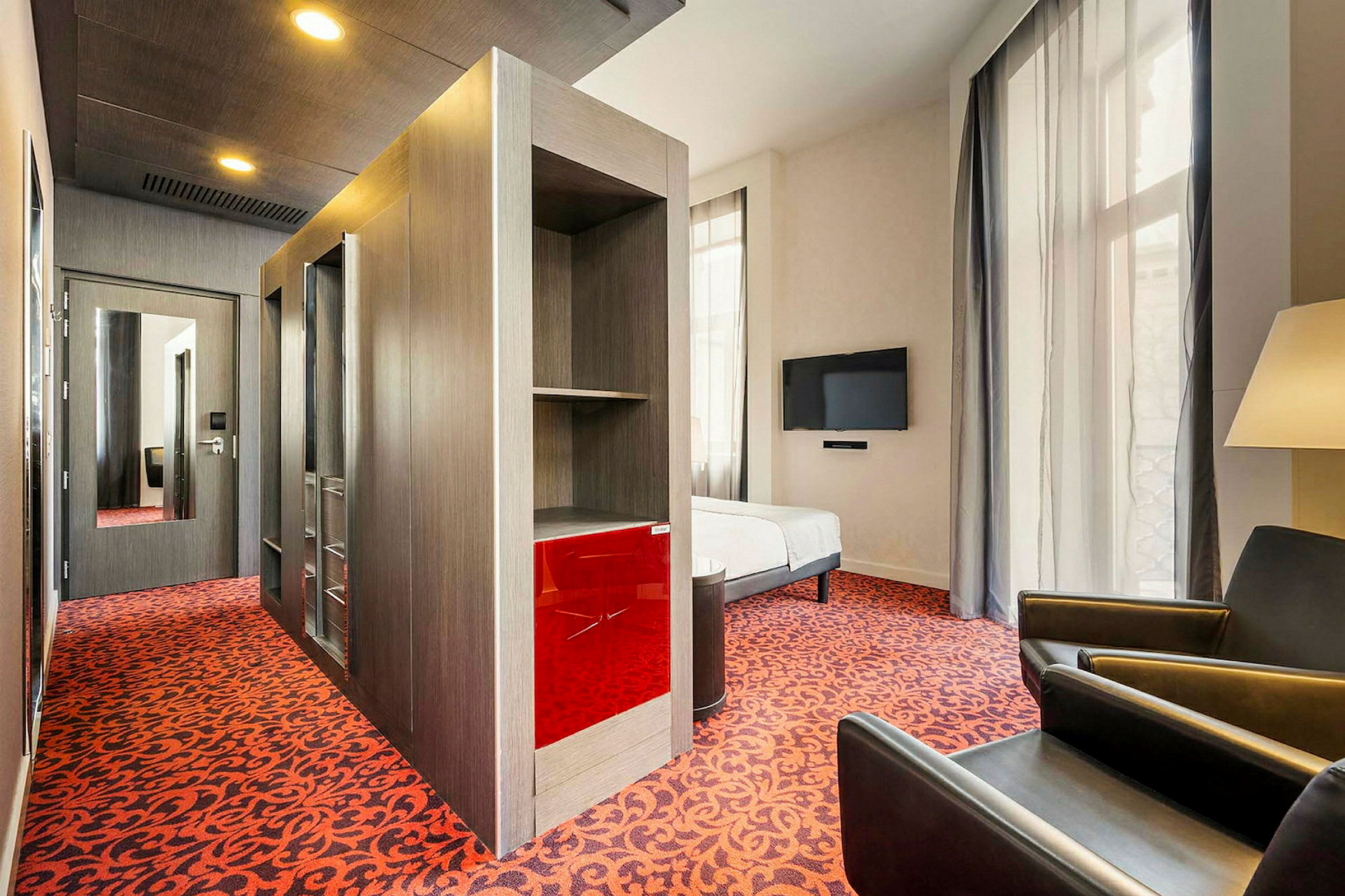 Hotelværelse med moderne indretning, et rødt tæppe og en vægmonteret TV. (AI-genereret tekst)