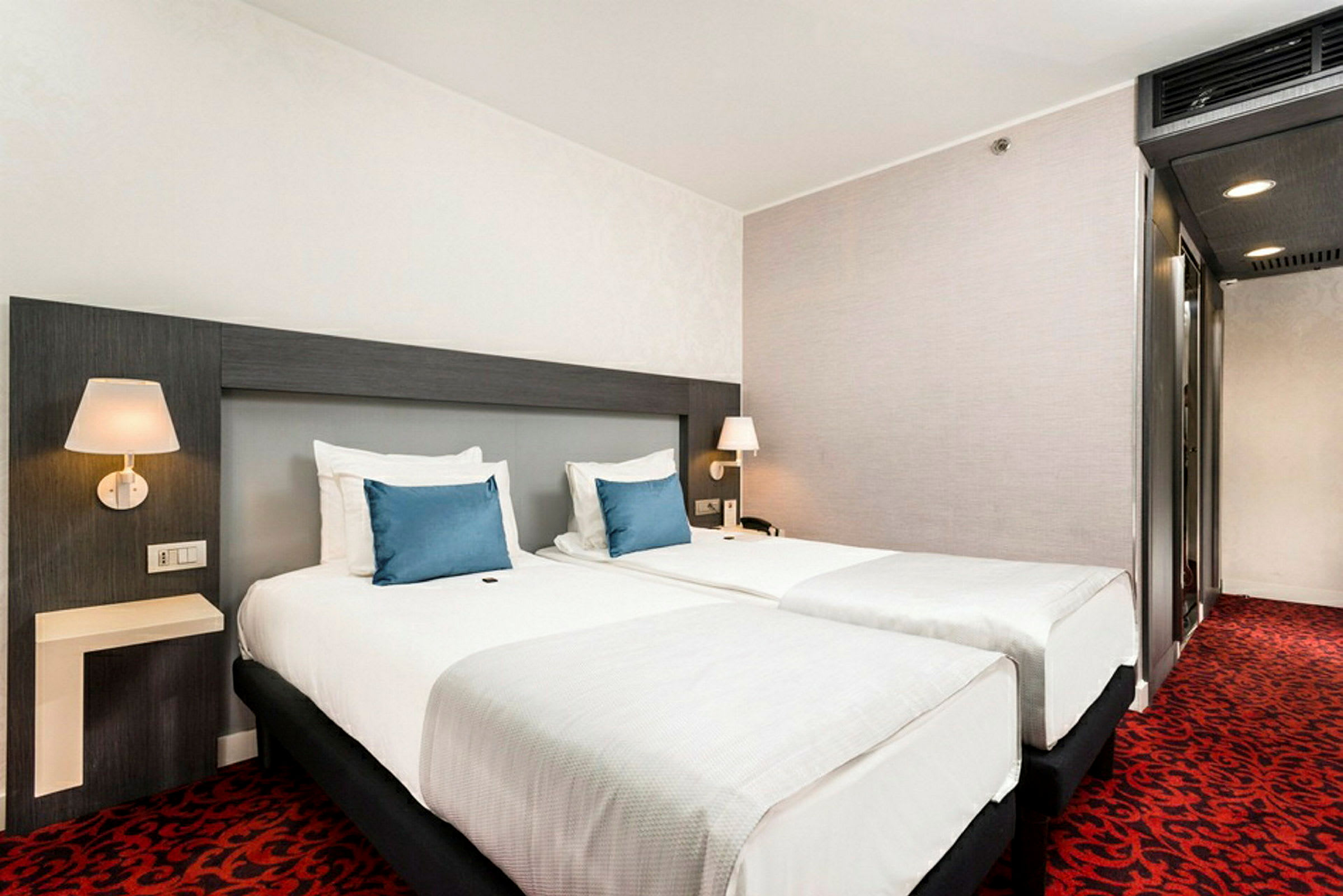 Hotelværelse med to separate senge og blå pyntepuder. (AI-genereret tekst)