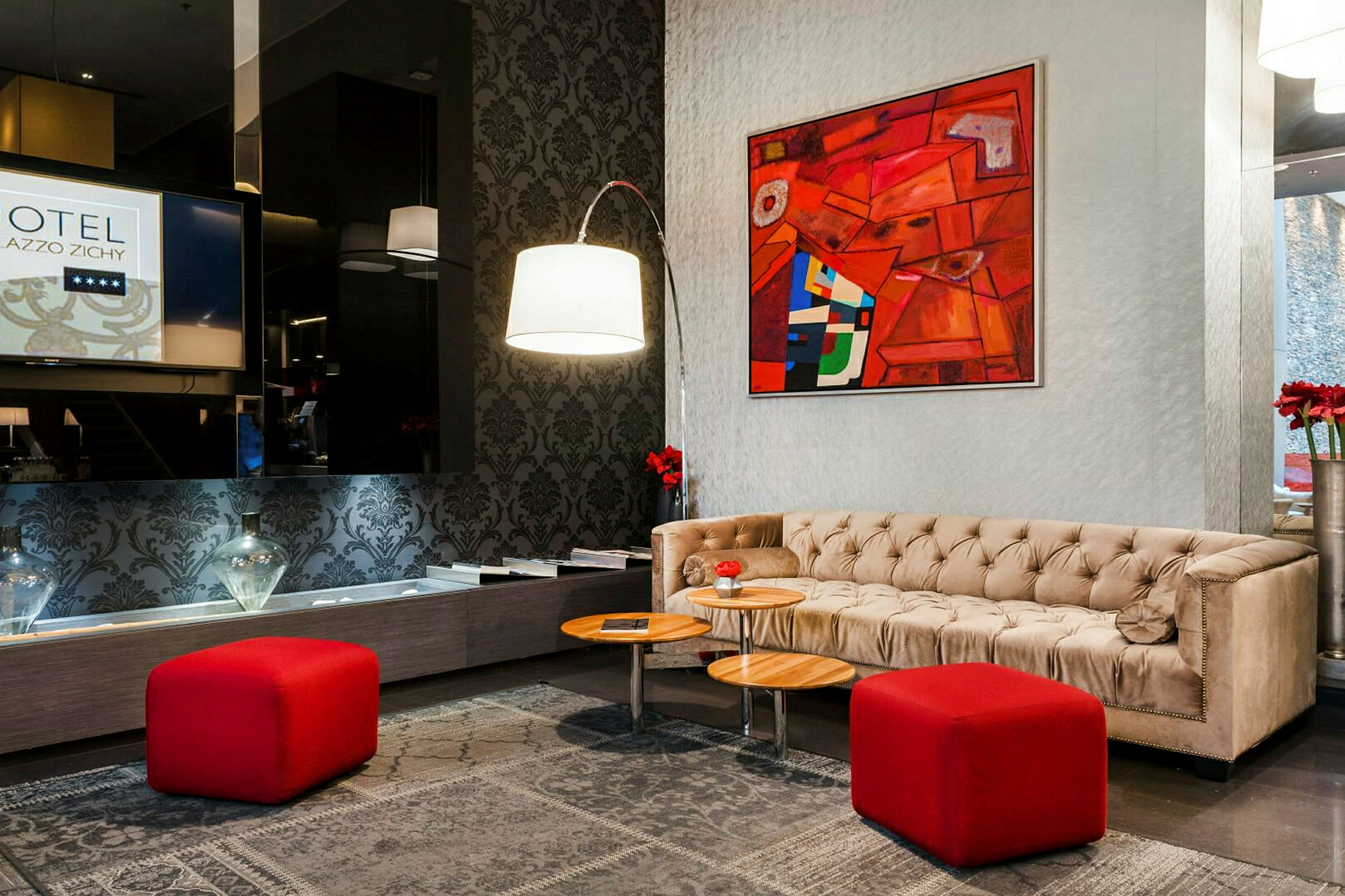 Et hotellobbyområde med en beige sofa, røde skamler og et abstrakt kunstværk på væggen. (AI-genereret tekst)