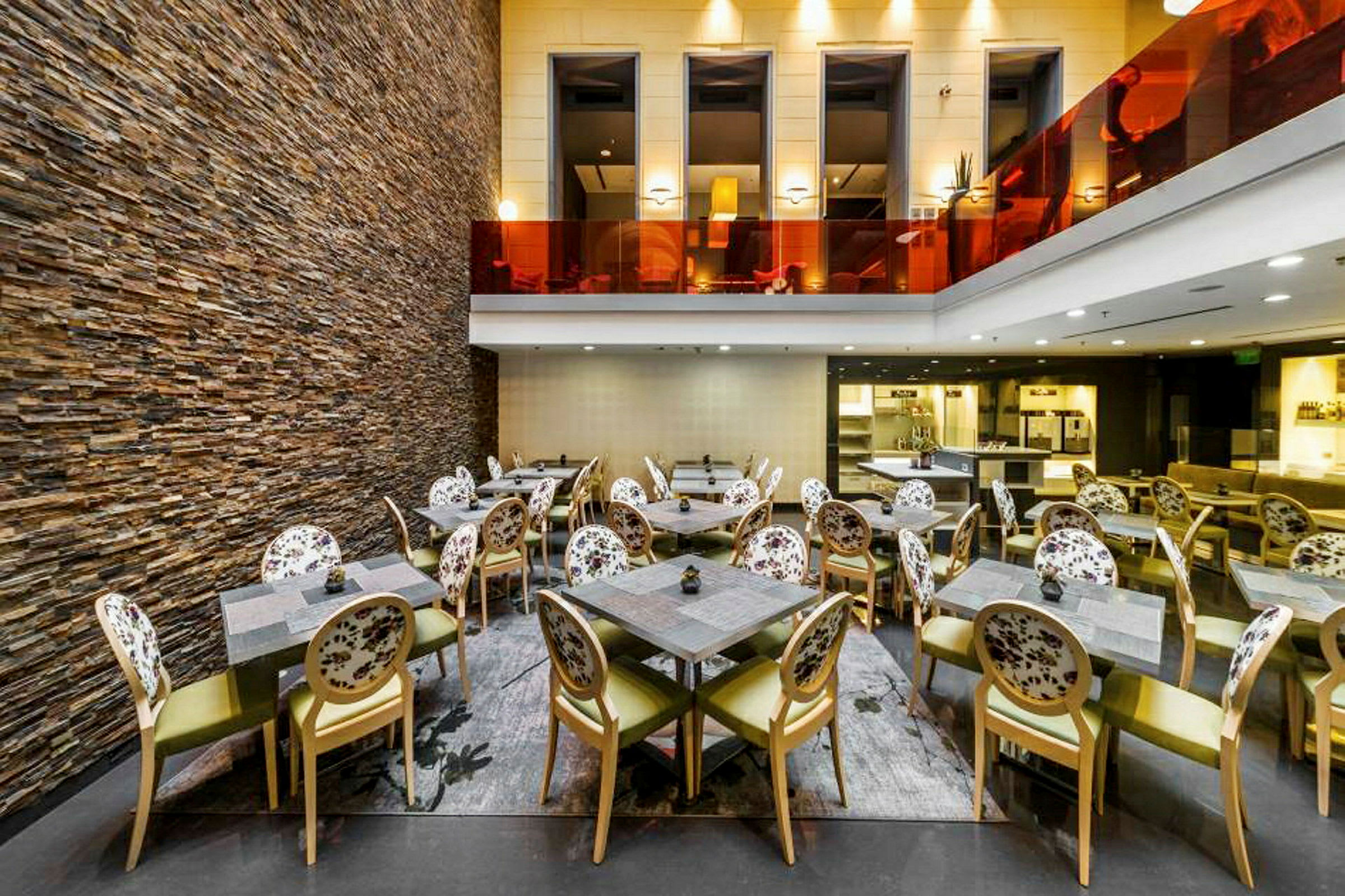 Interiør af en restaurant med stole og borde samt en væg af sten. (AI-genereret tekst)