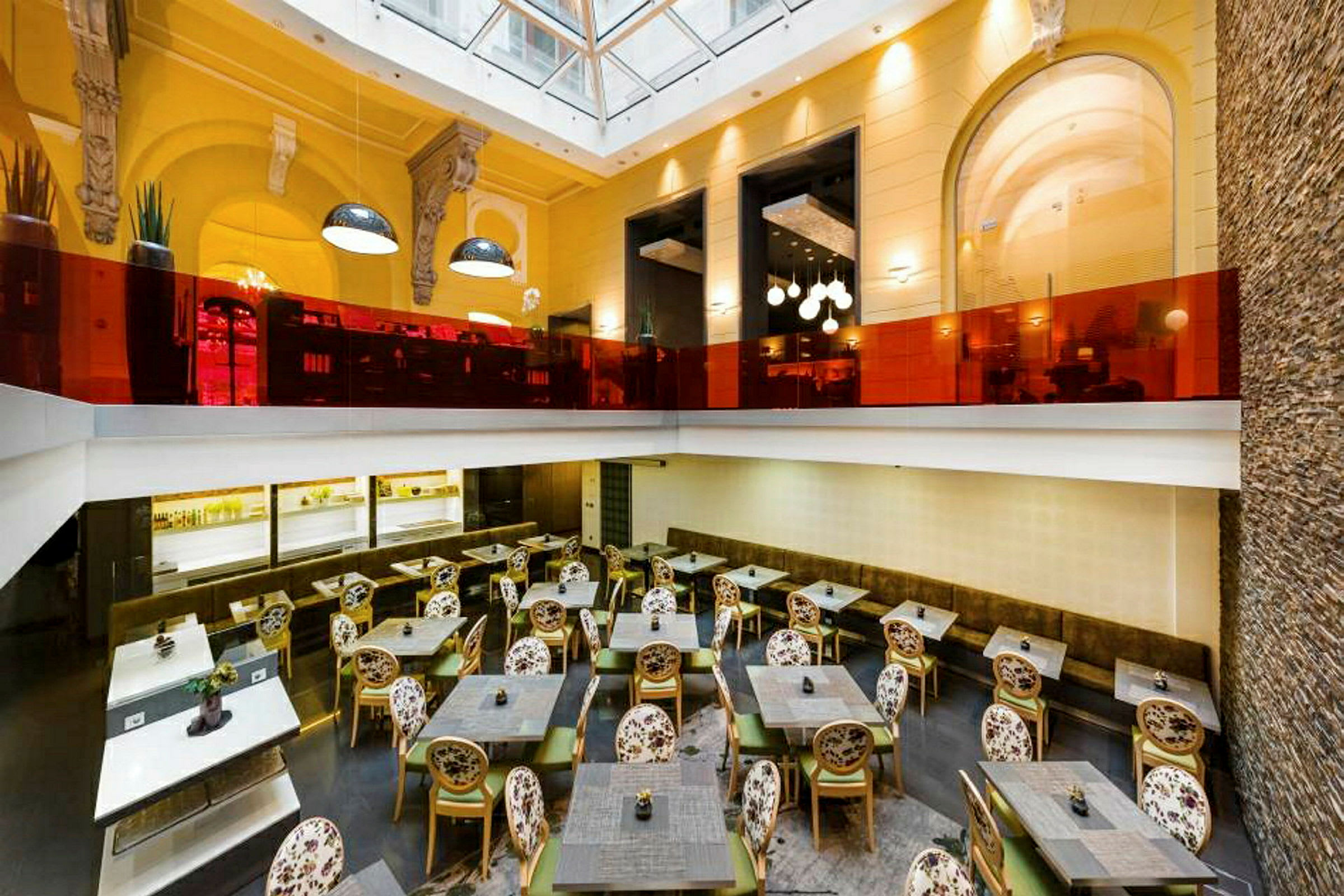 Et restaurantområde med borde, stole og en øvre etage indrettet med forskellige lamper og glasdetaljer. (AI-genereret tekst)