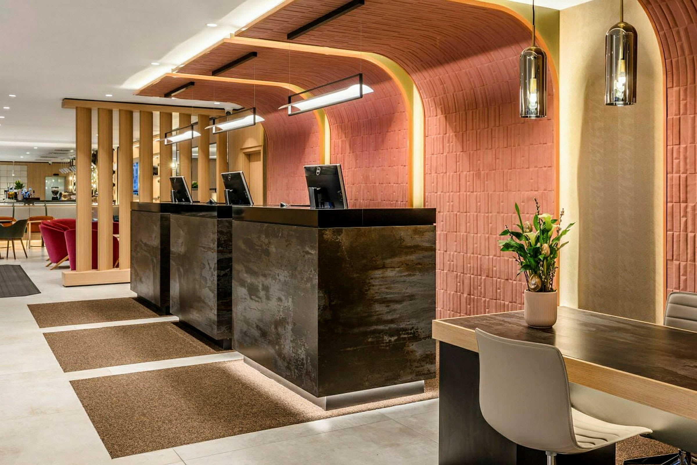 Receptionen på et hotel med moderne møbler og indretning, tre diske med computerskærme samt en siddegruppe i baggrunden. (AI-genereret tekst)