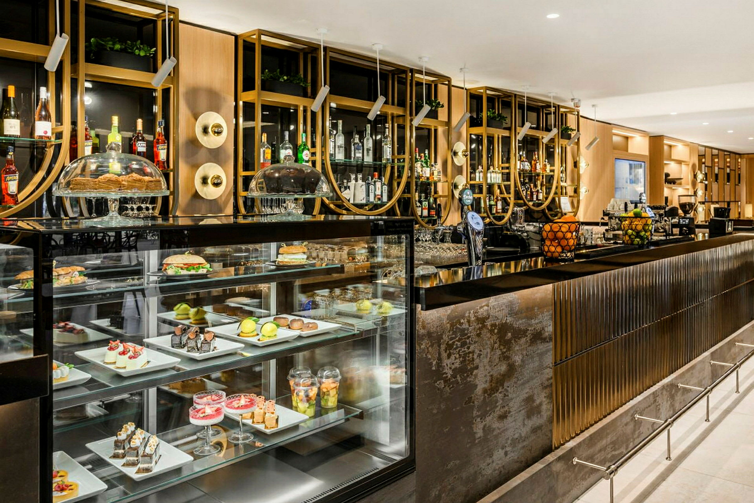 En elegant bardisk med indbyggede glasmontrer, der viser forskellige desserter og frugter. Bag baren ses hylder med spiritusflasker og dekorative detaljer. (AI-genereret tekst)