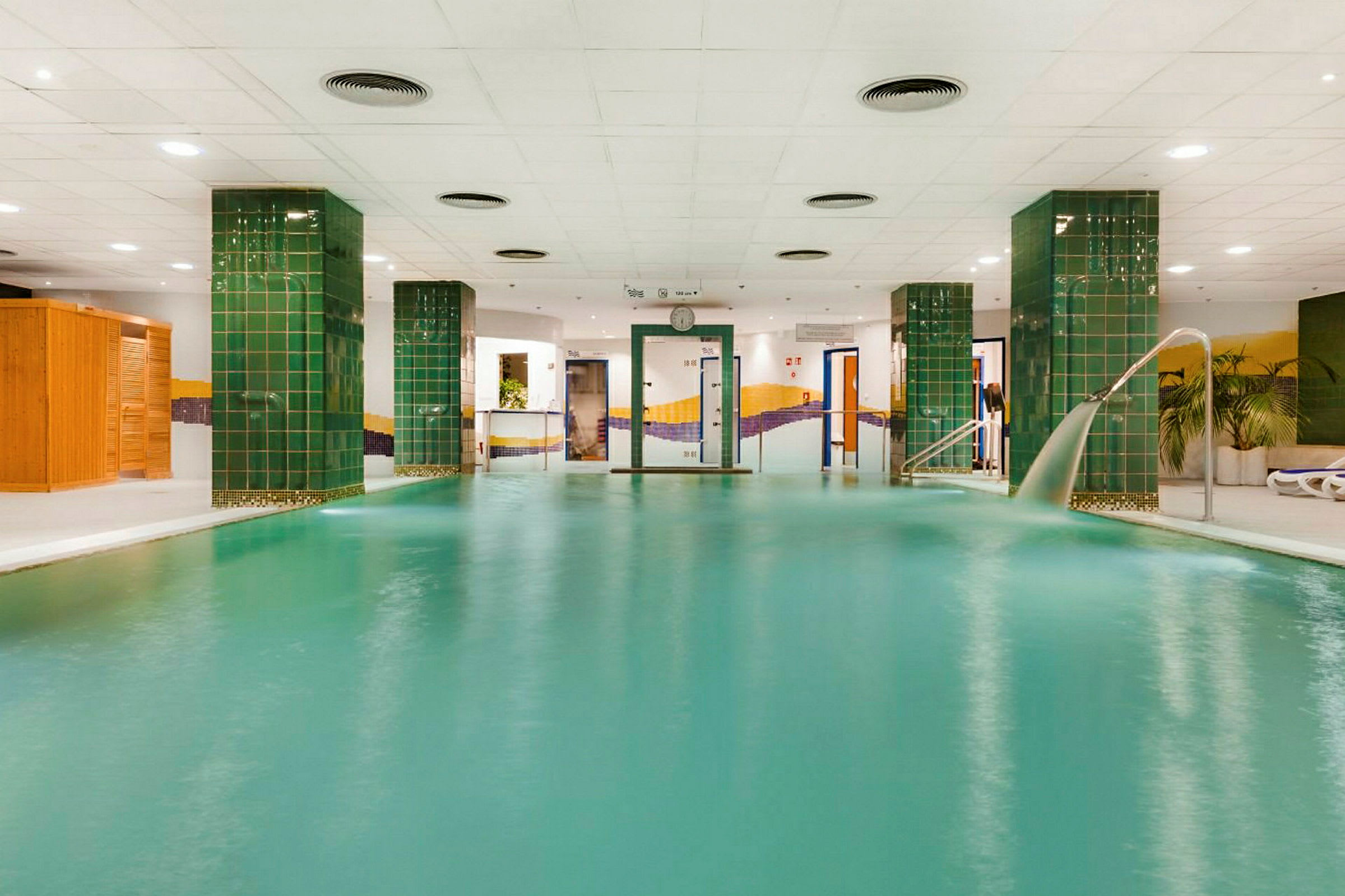 En indendørs swimmingpool med grønne søjler og hvidt loft. (AI-genereret tekst)