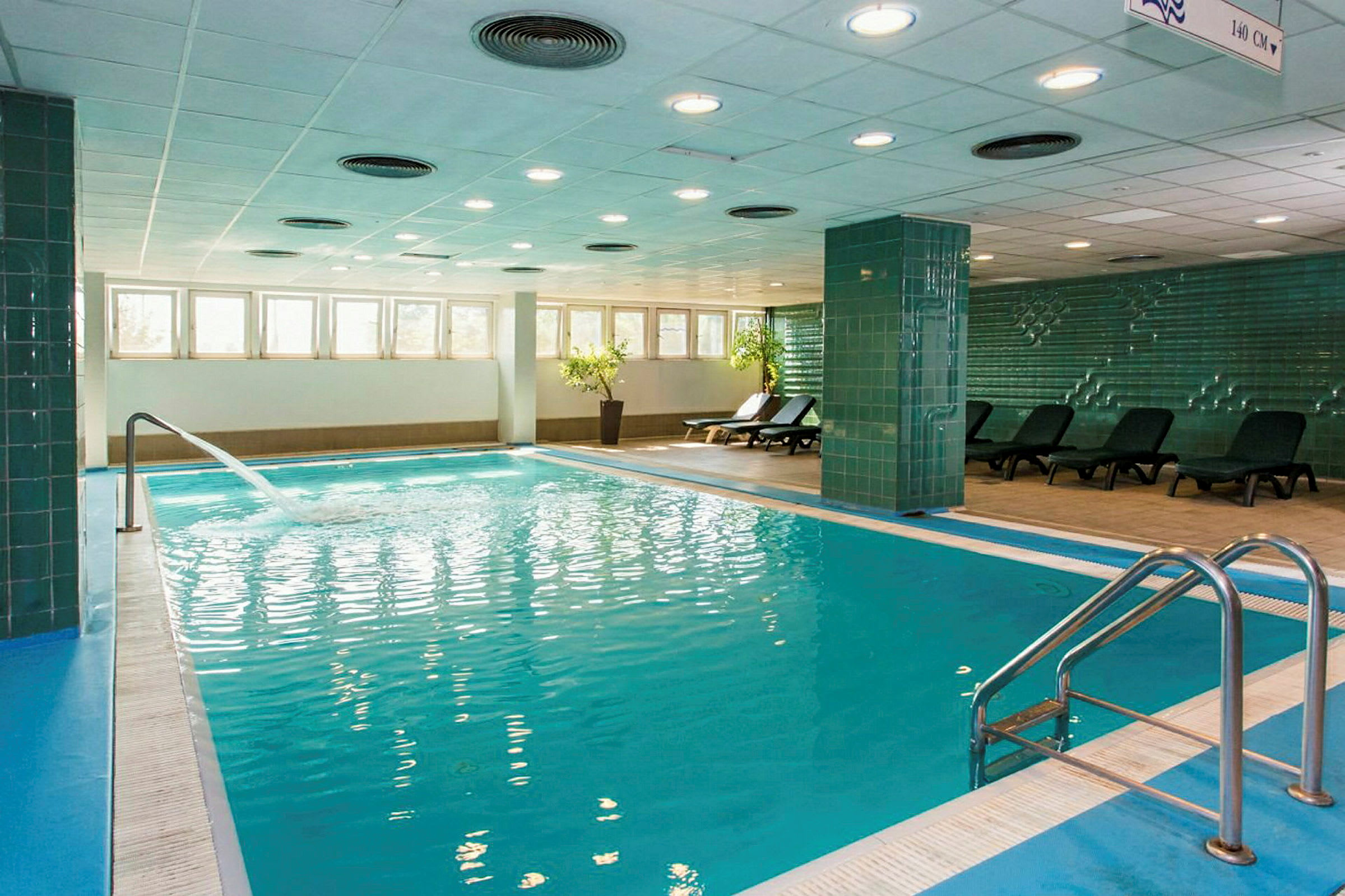 Indendørs swimmingpool med liggestole ved siden og en fontæne, der løber ind i vandet. (AI-genereret tekst)