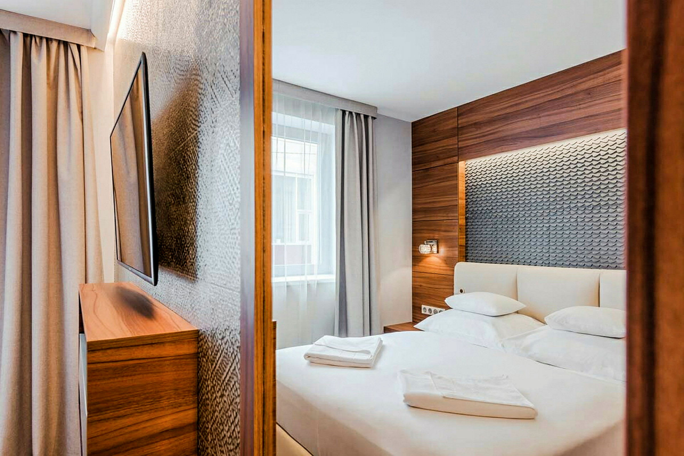Et moderne hotelværelse med en stor seng, dekoreret med træpaneler og mønstret væg bag sengens gavl. (AI-genereret tekst)
