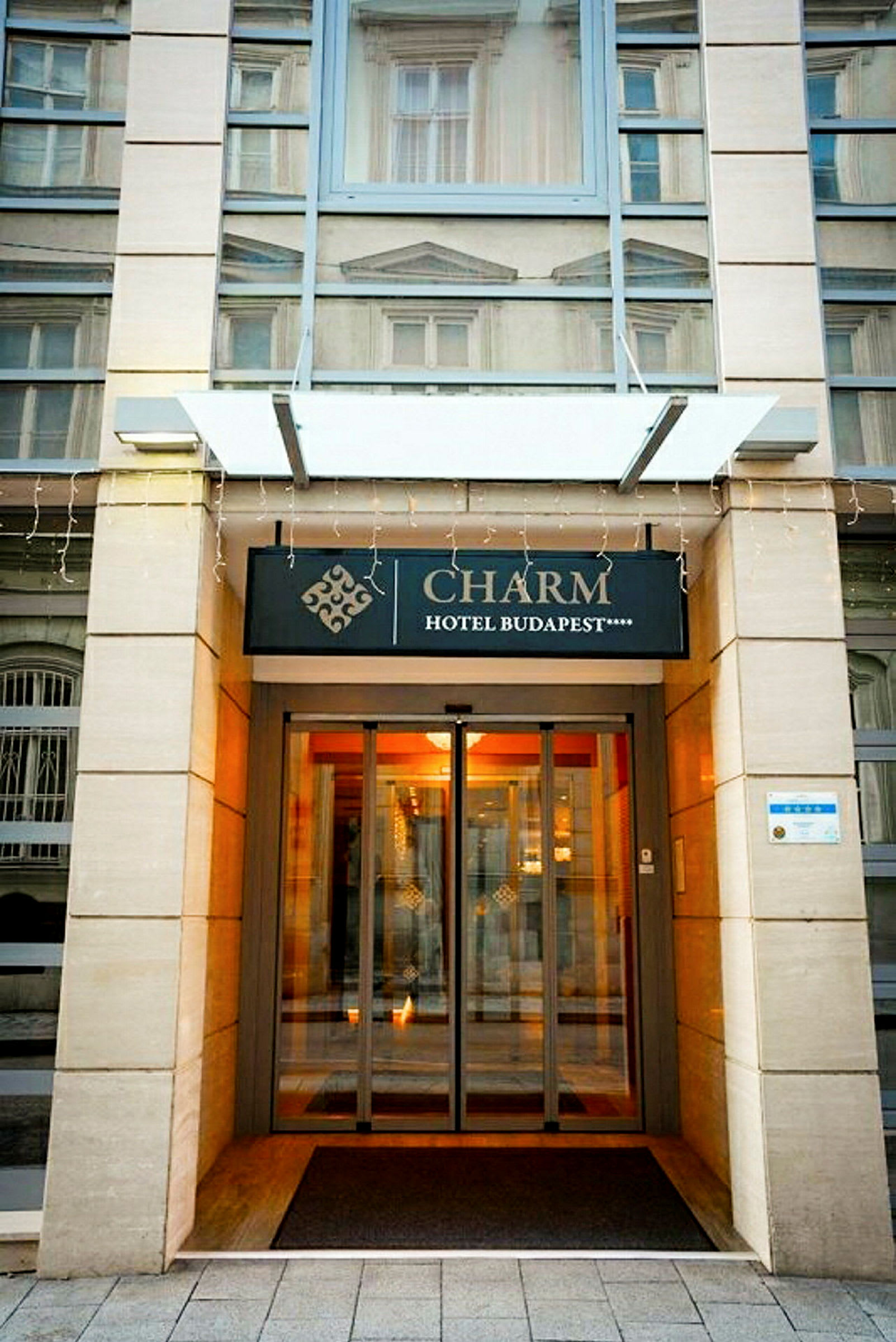 Indgangen til Charm Hotel Budapest med skilt og glasdøre. (AI-genereret tekst)