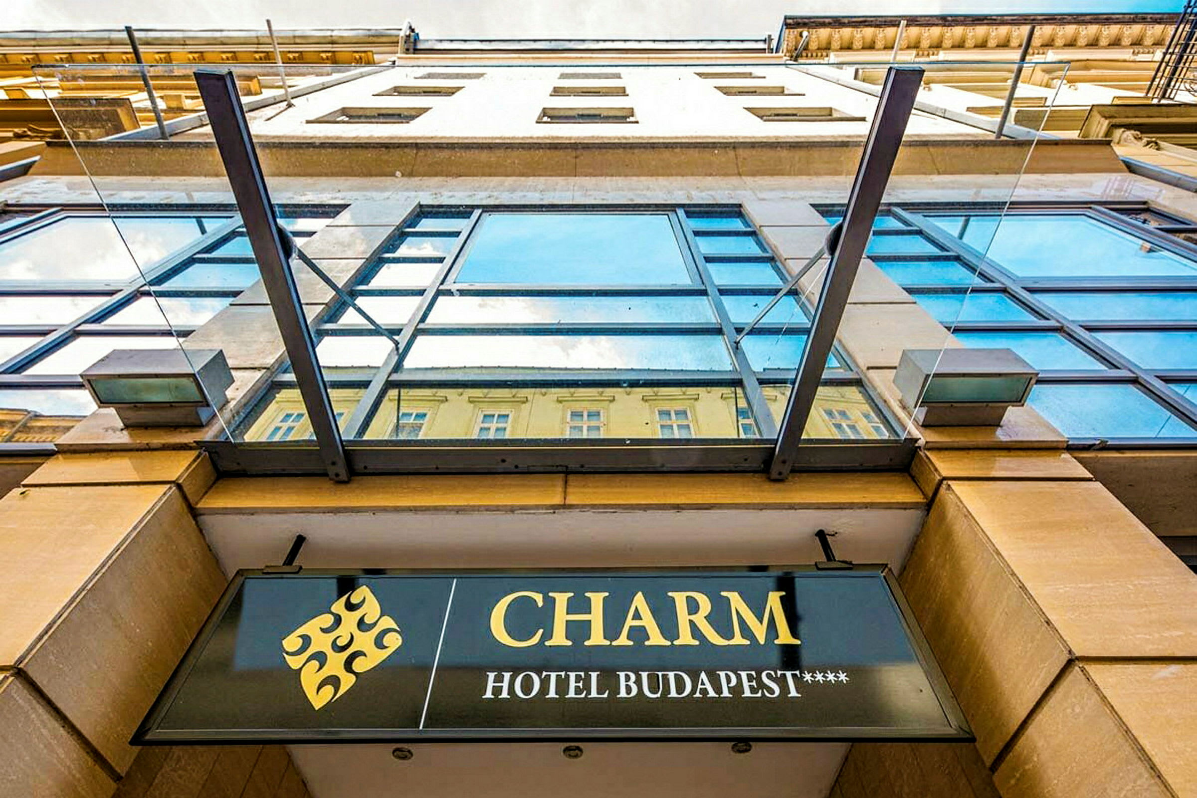 Facadebillede af en bygning med et skilt, der viser navnet "CHARM Hotel Budapest****". (AI-genereret tekst)