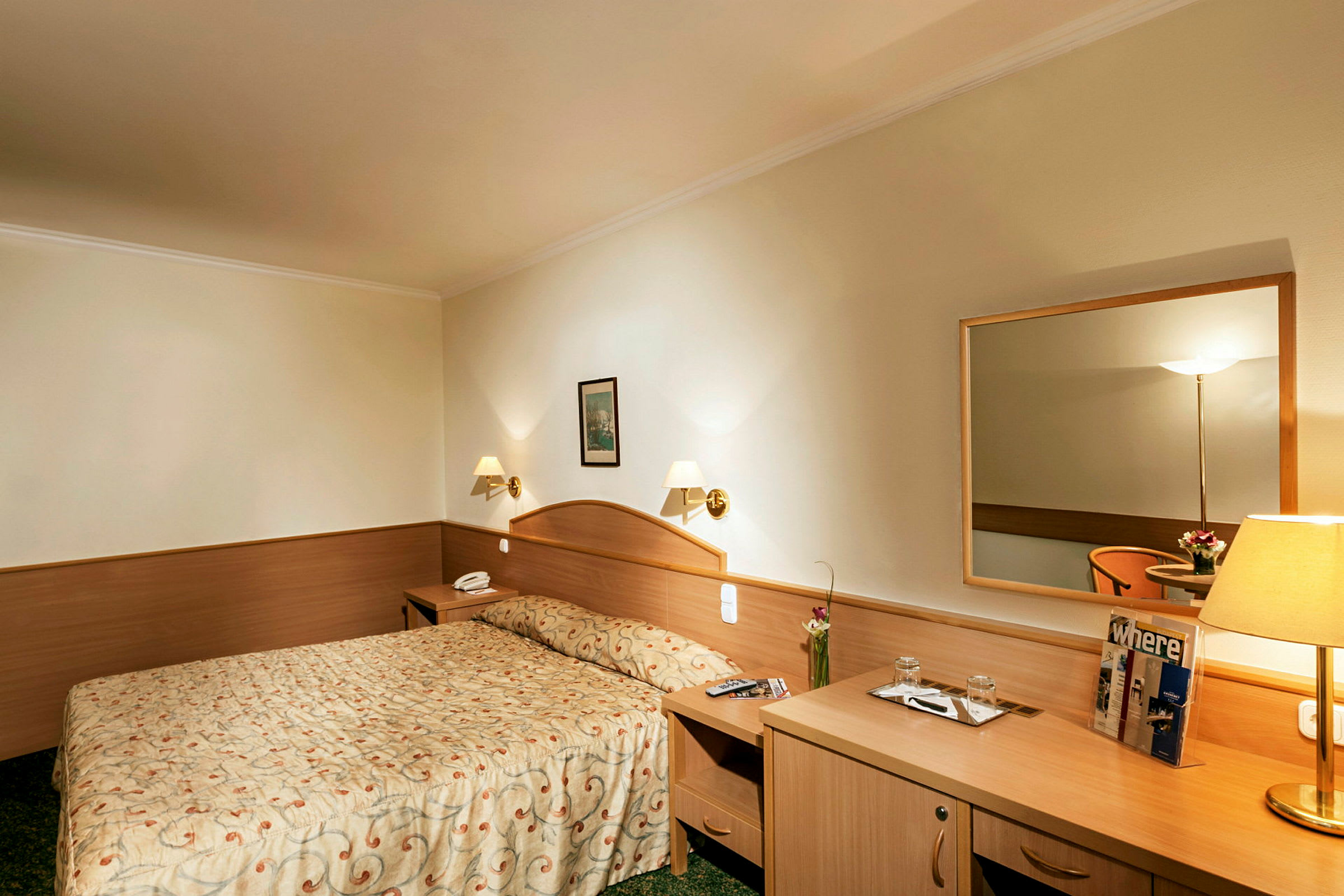 Hotelværelse med dobbeltseng, natbord, spejl og skrivebord. (AI-genereret tekst)