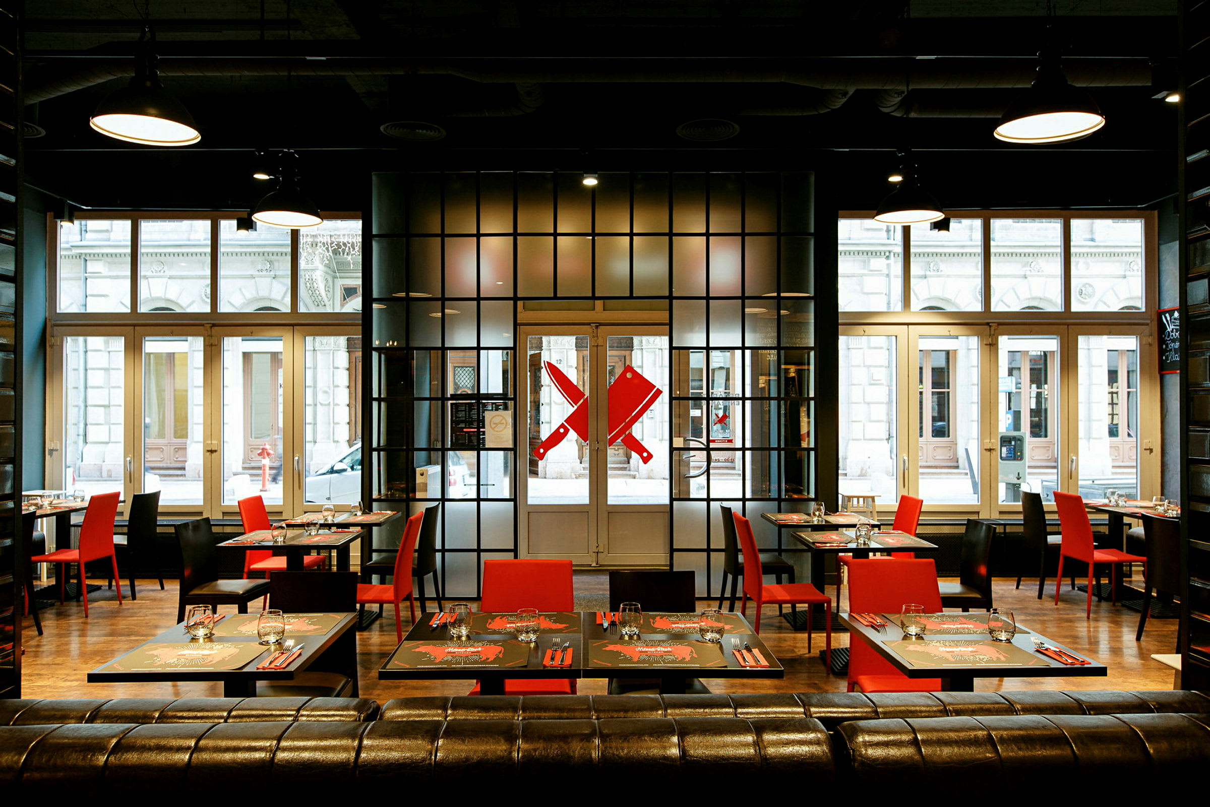 Moderne restaurant med røde og sorte stole samt dækkede borde foran store vinduer. (AI-genereret tekst)
