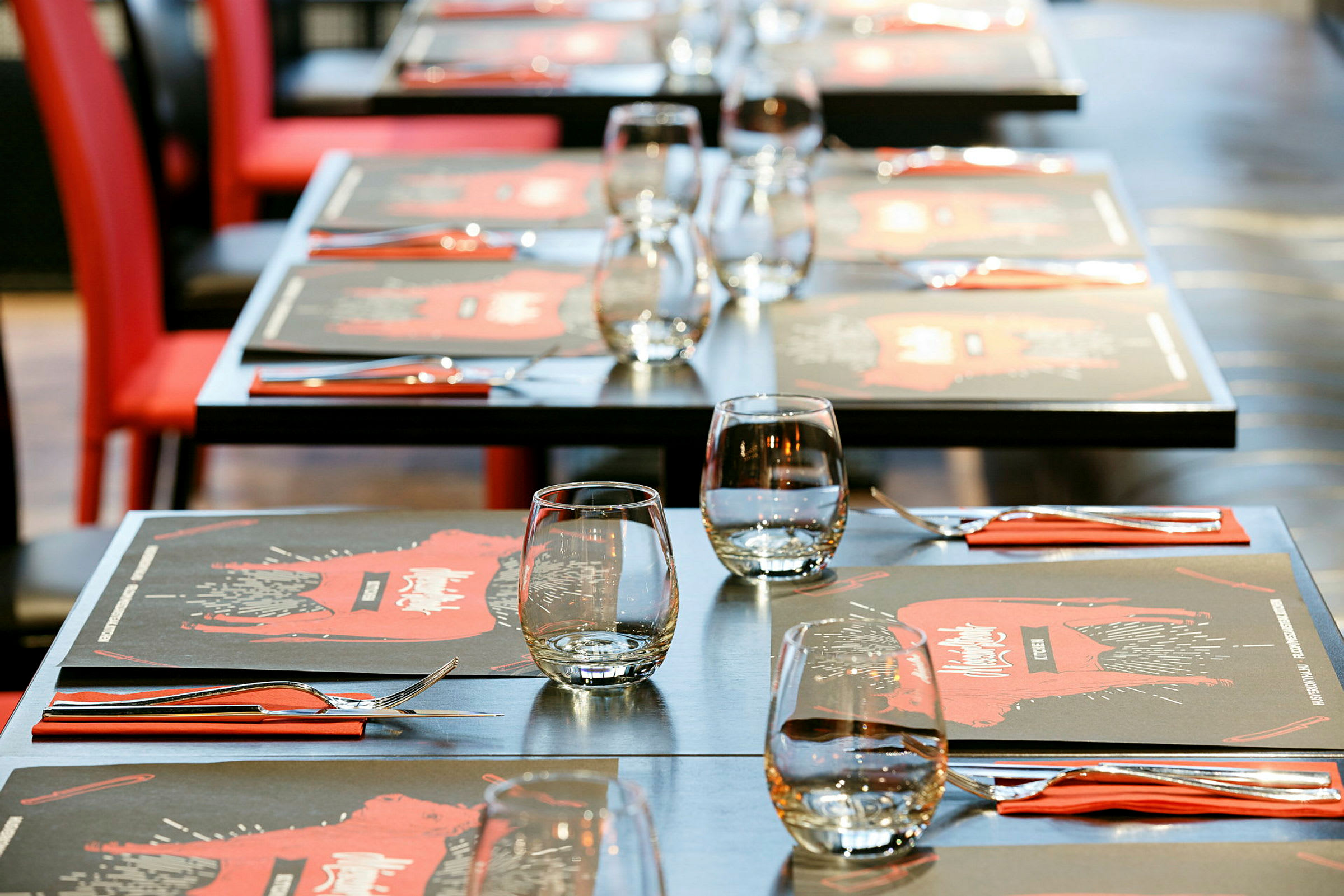 Opstillede borde med glas, bestik og røde servietter, restaurantmiljø. (AI-genereret tekst)