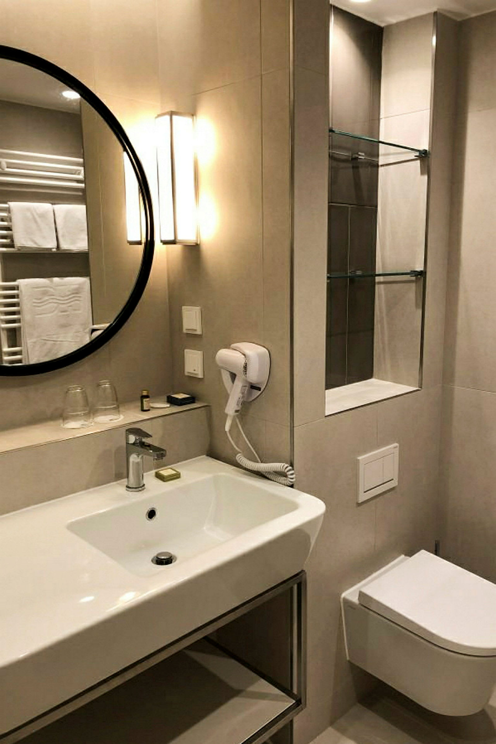 Et badeværelse med en hvid håndvask, spejl, hårtørrer og toilet. (AI-genereret tekst)