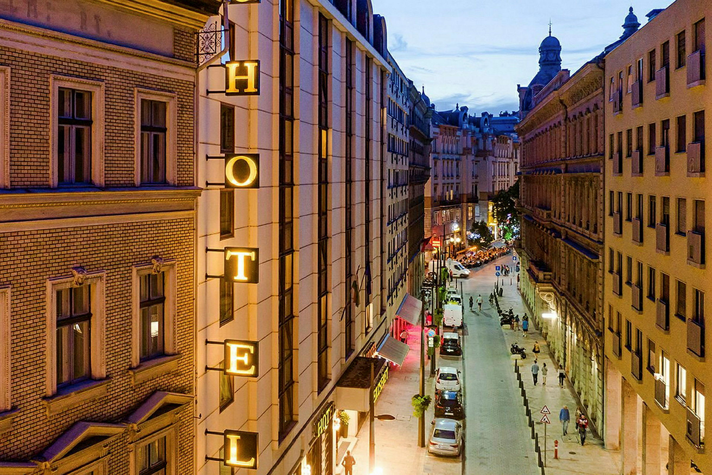 Billede af en bygade om aftenen med et hotelskilt på en bygning. (AI-genereret tekst)