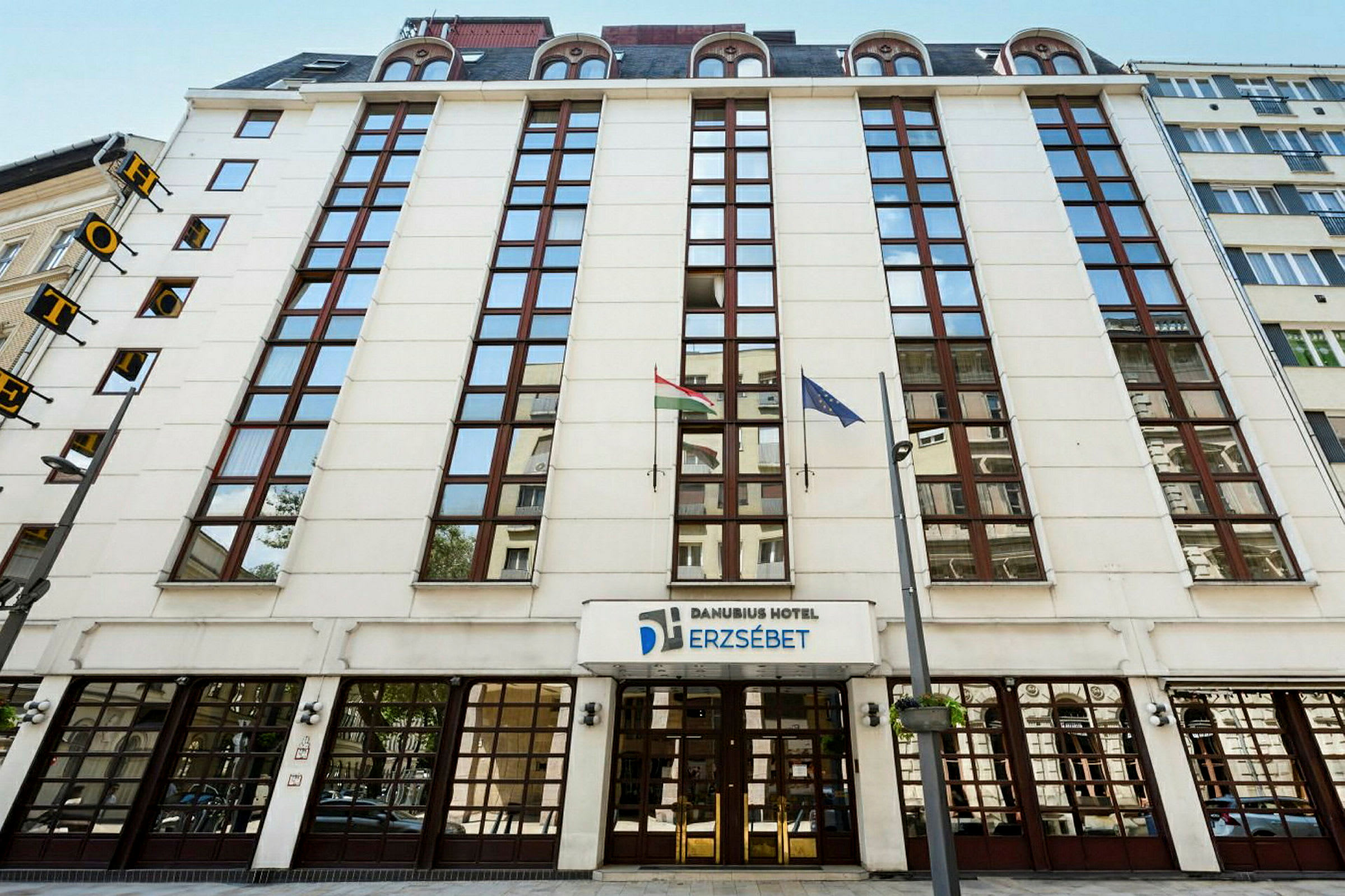 Forsiden af Danubius Hotel Erzsébet med glasruder og flag. (AI-genereret tekst)
