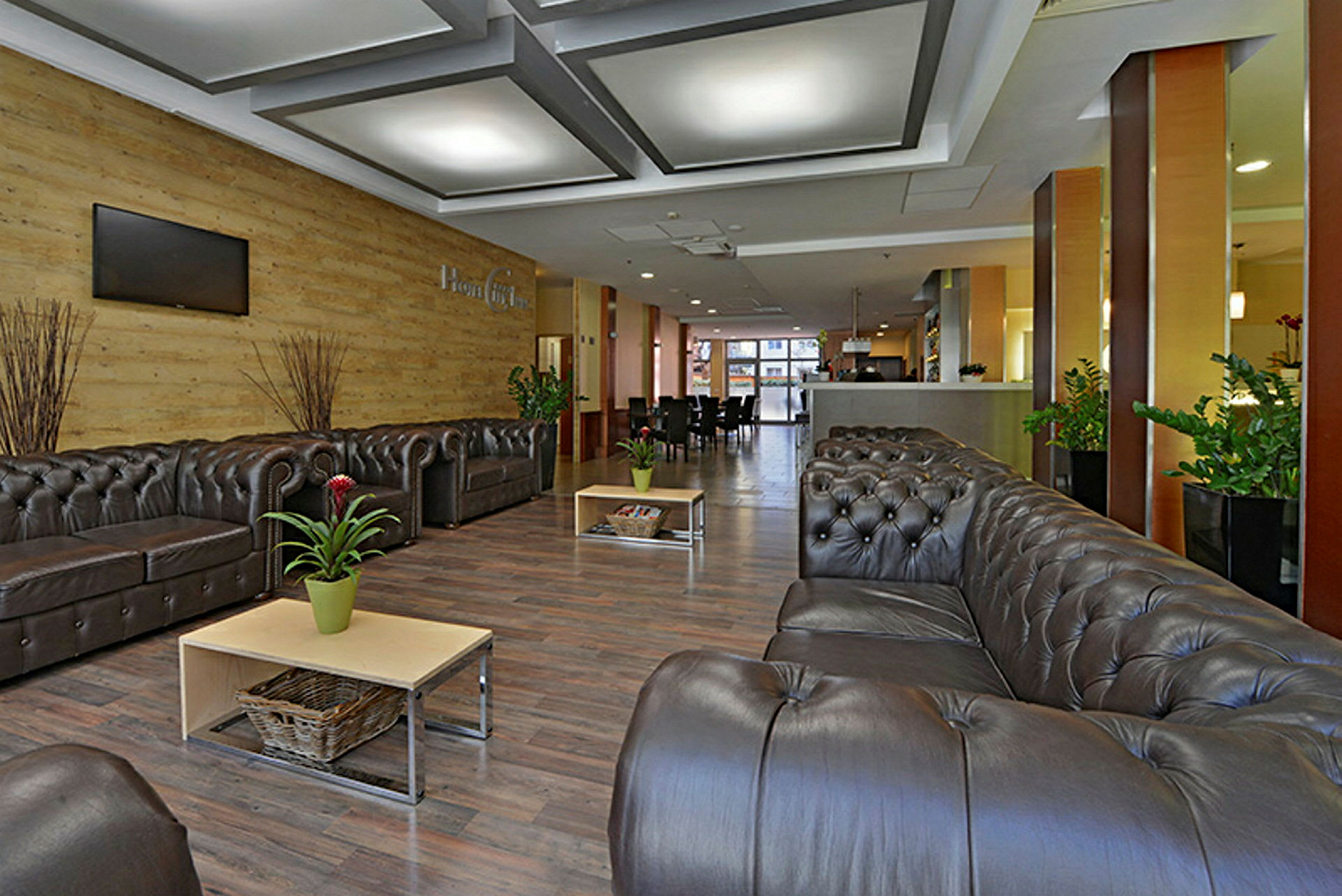 En hotellobby med komfortable sofaer, sofaborde, potteplanter og moderne interiør. (AI-genereret tekst)
