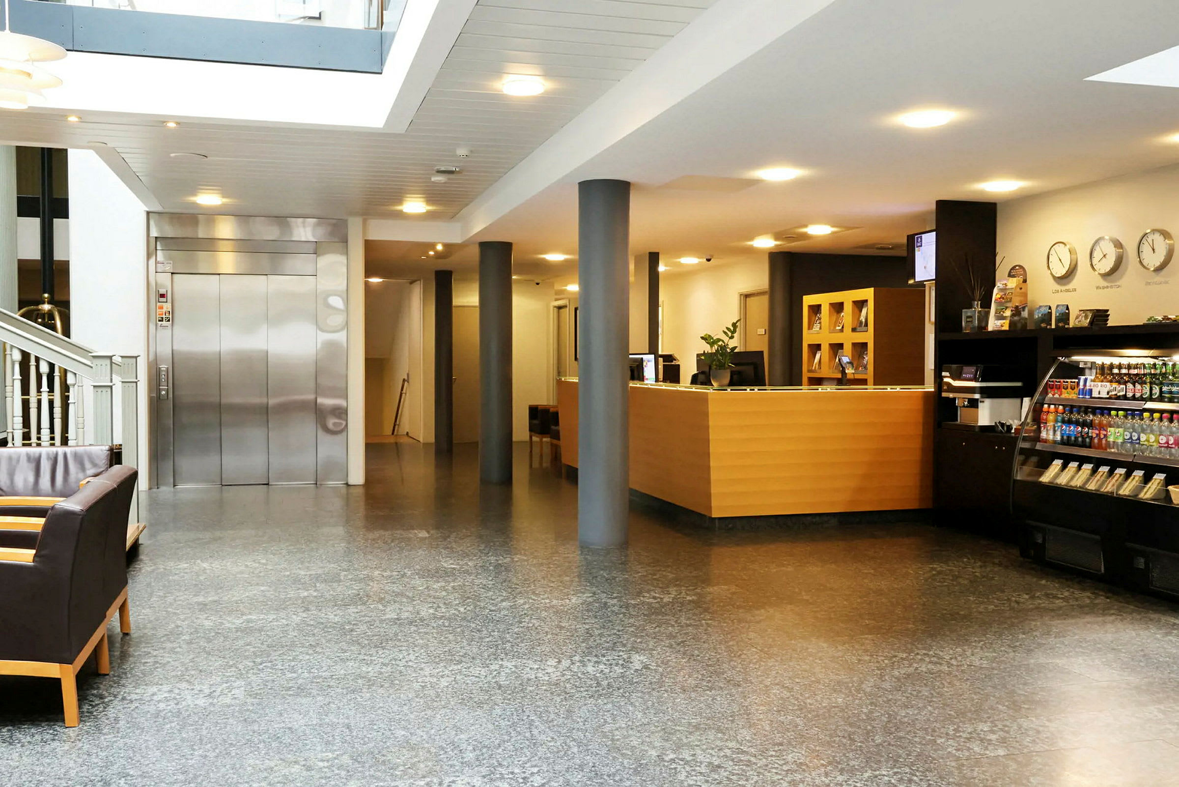 Et hotelreceptionsområde med en reception, en elevator, sofaer og en lille butik. (AI-genereret tekst)