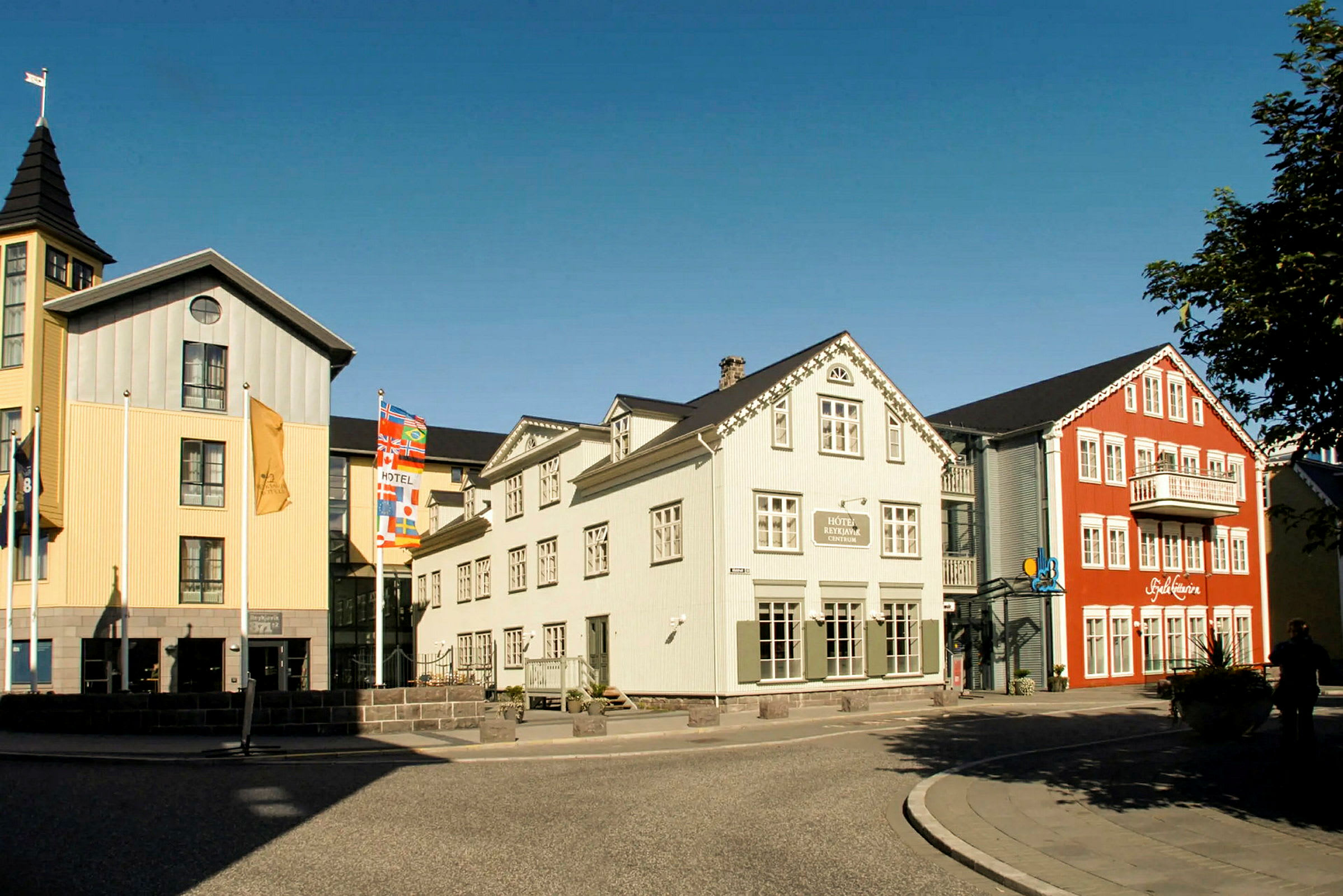 Billede af farverige bygninger med hotel og restaurant nær en gade med fortov. (AI-genereret tekst)