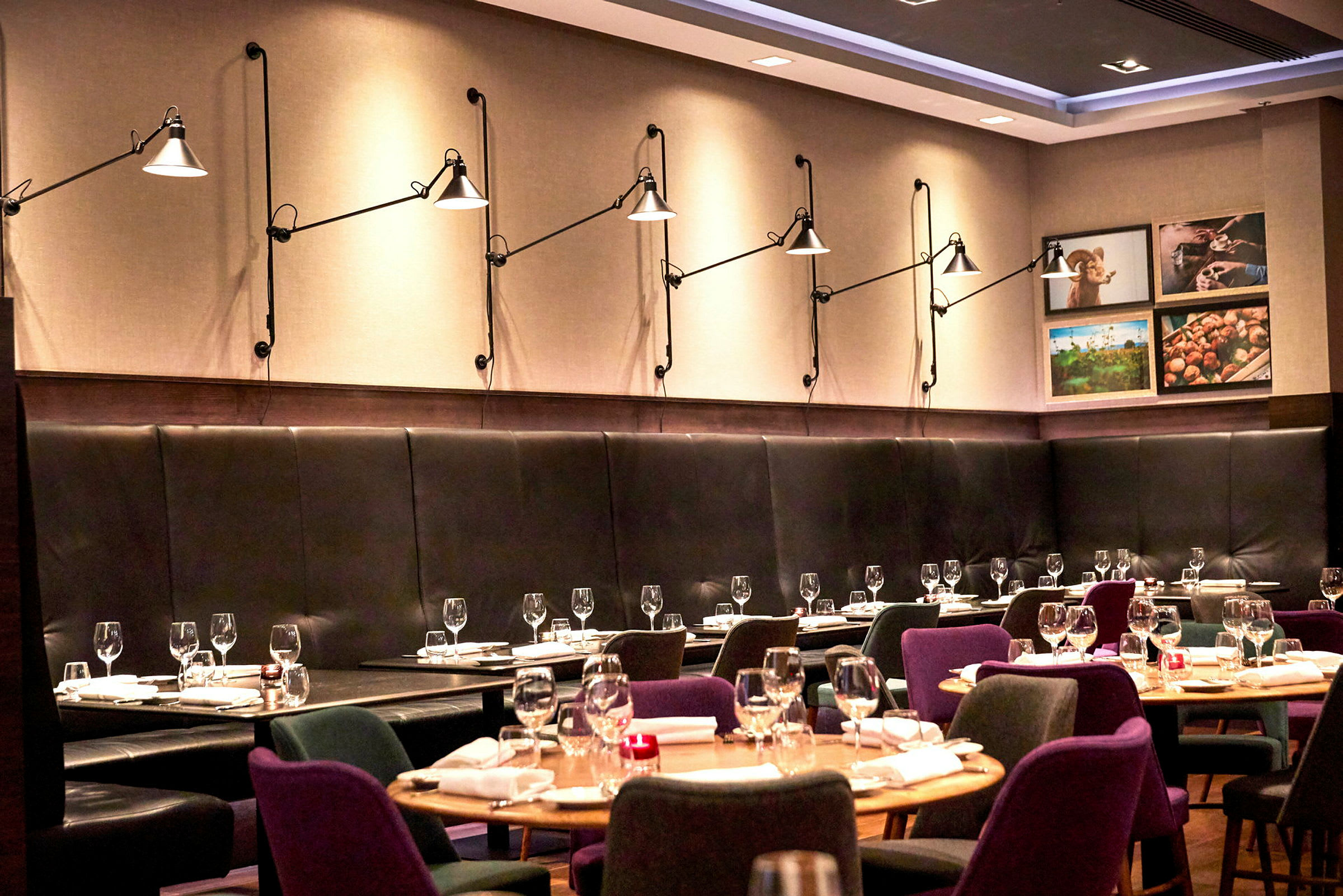 En moderne restaurant med opdækkede borde og stole samt vægbelysning på en polstret væg. (AI-genereret tekst)