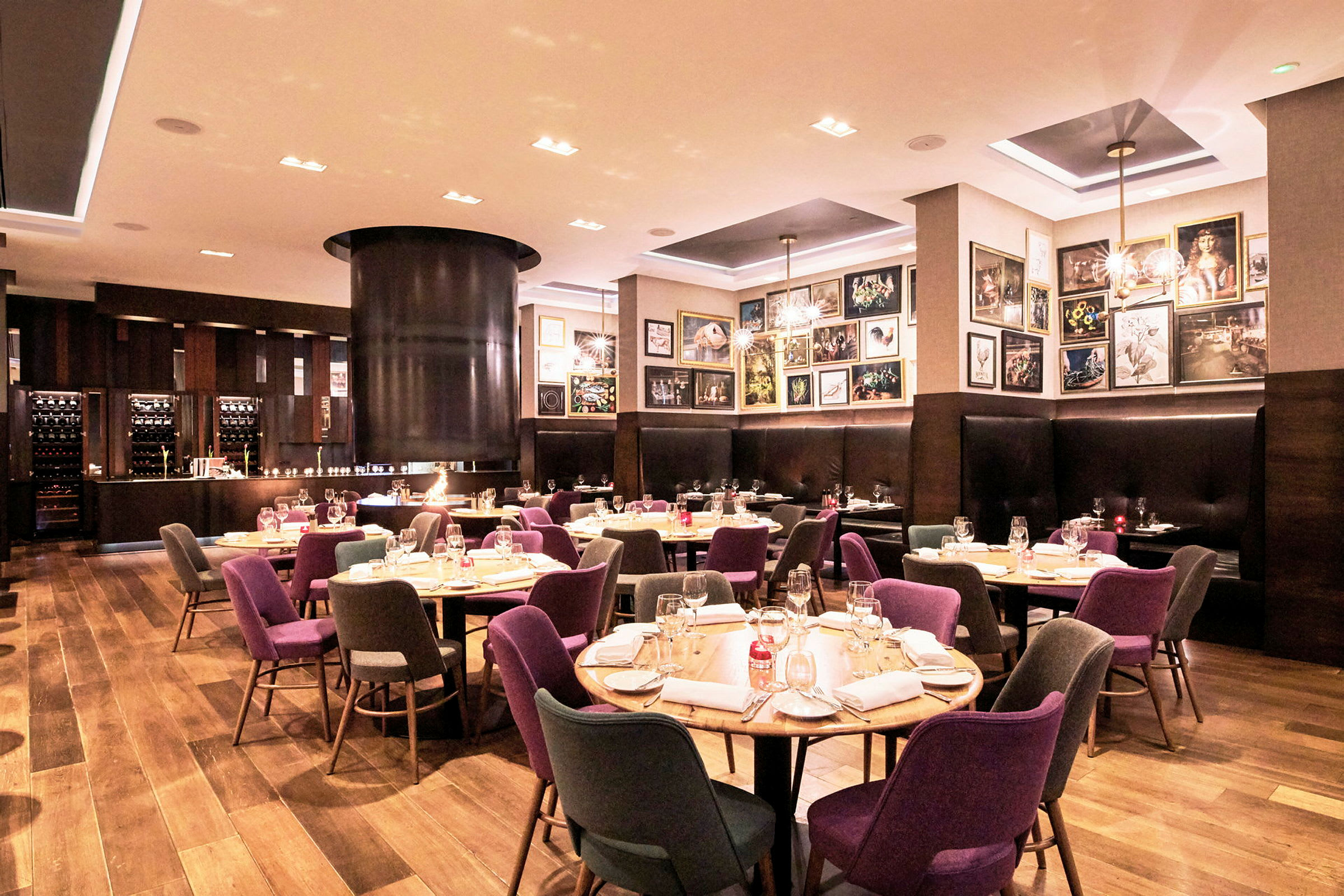 Et veloplyst restaurantinteriør med opdækkede borde, farverige stole og en hyggelig atmosfære. (AI-genereret tekst)
