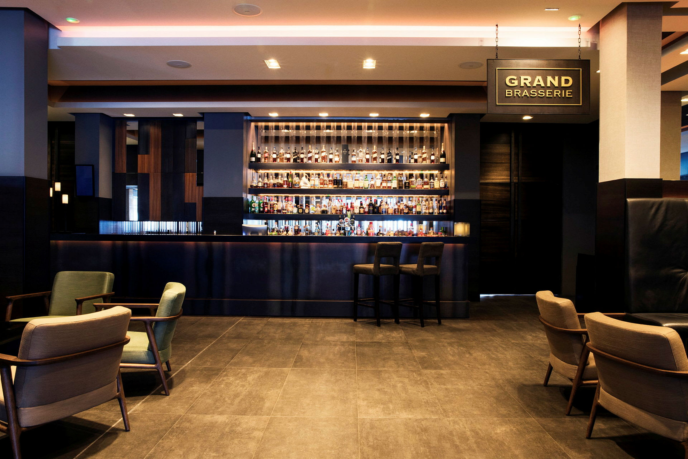 En moderne hotelbar med en oplyst bardisk og forskellige spiritusflasker synlige på hylderne bagved. (AI-genereret tekst)