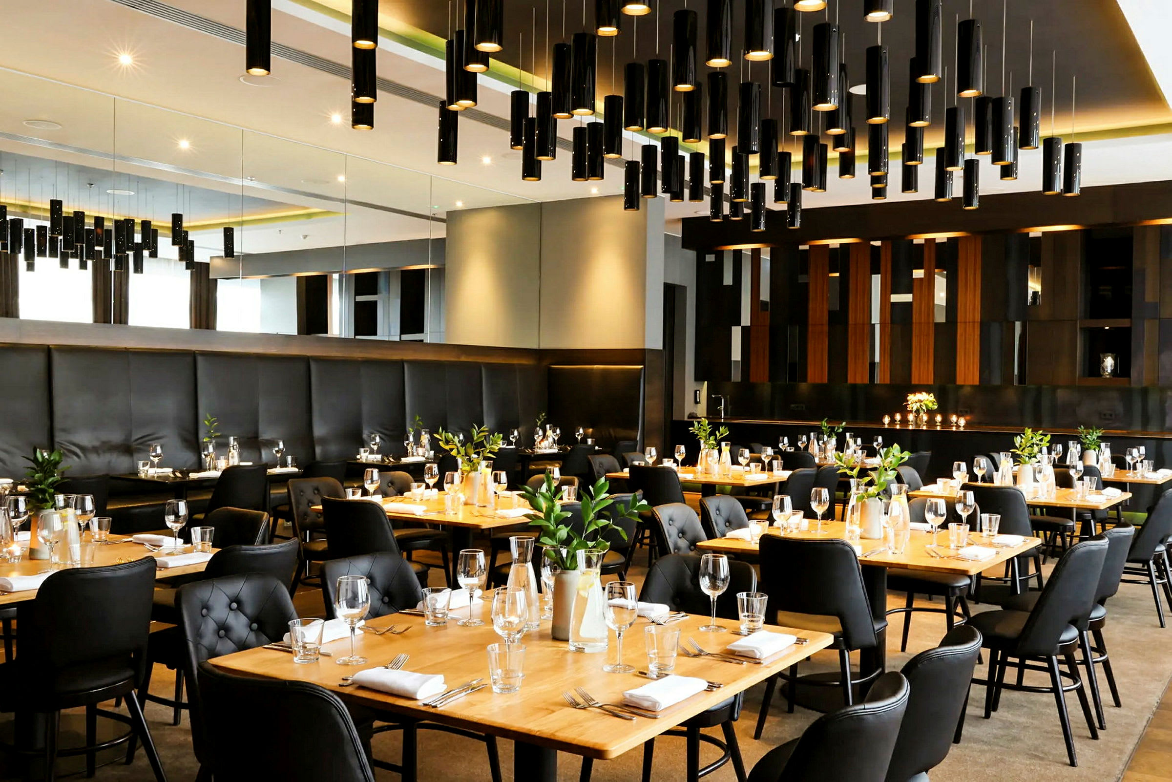 En elegant restaurant med dækkede borde, sorte stole og træborde samt moderne lysdesign. (AI-genereret tekst)