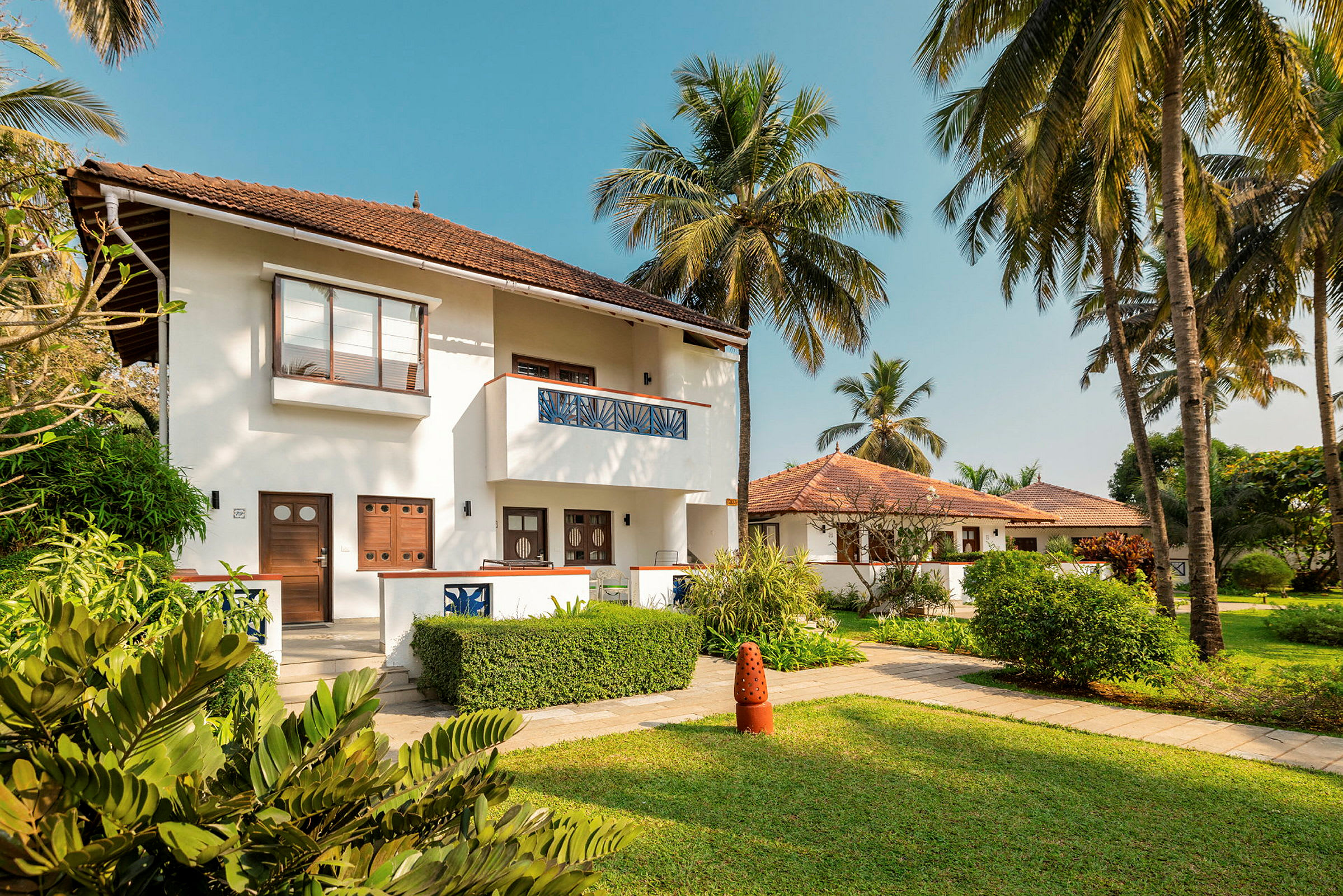 Et hvidt to-etagers hus med brunt tag og en frodig have, omgivet af palmer. (AI-genereret tekst)